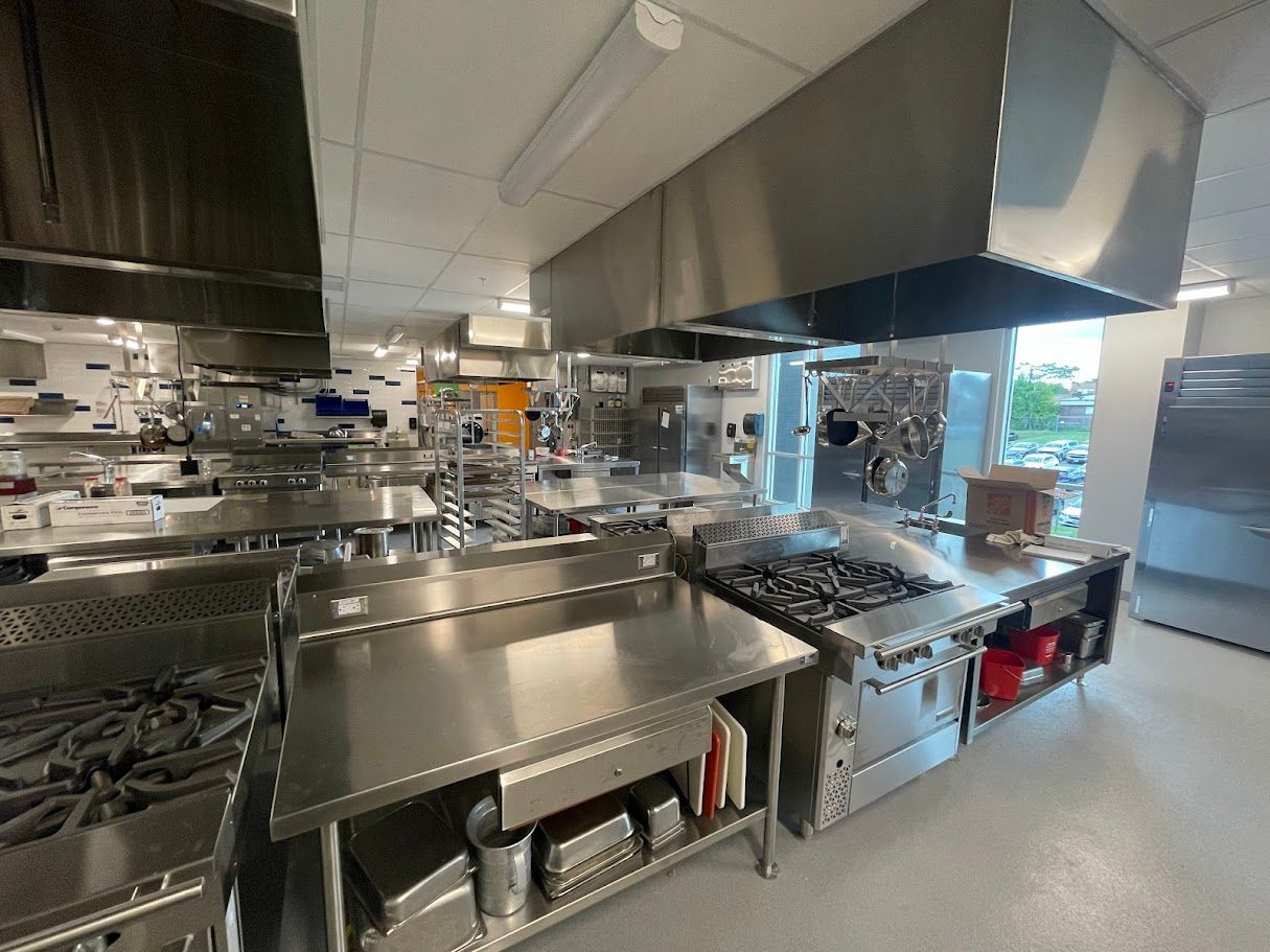 A professional commercial kitchen featuring stainless steel prep tables, gas ranges, and overhead ventilation hoods.