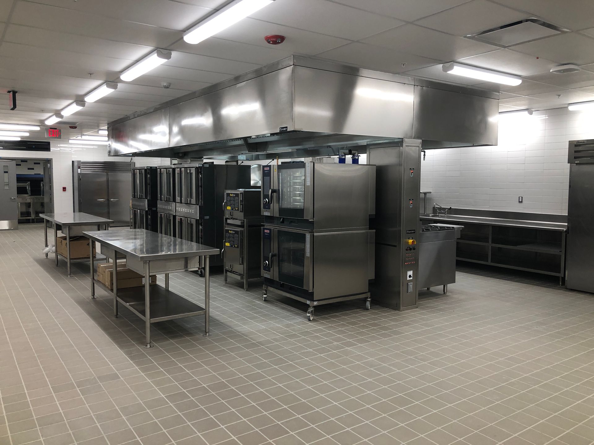 A commercial kitchen with stainless steel appliances, prep tables, and a large overhead ventilation hood.