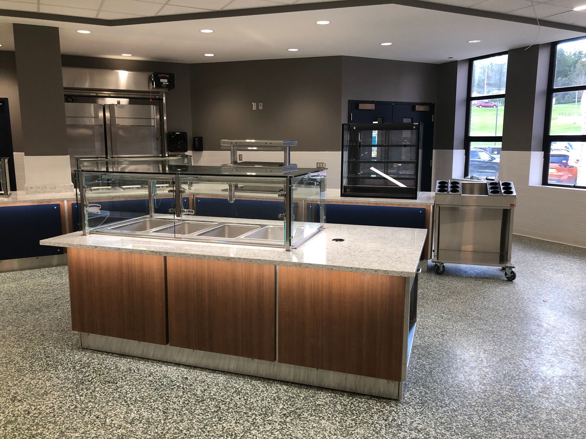 A food serving station with a stainless steel buffet counter and stone top, featuring wood paneling, in a modern interior.