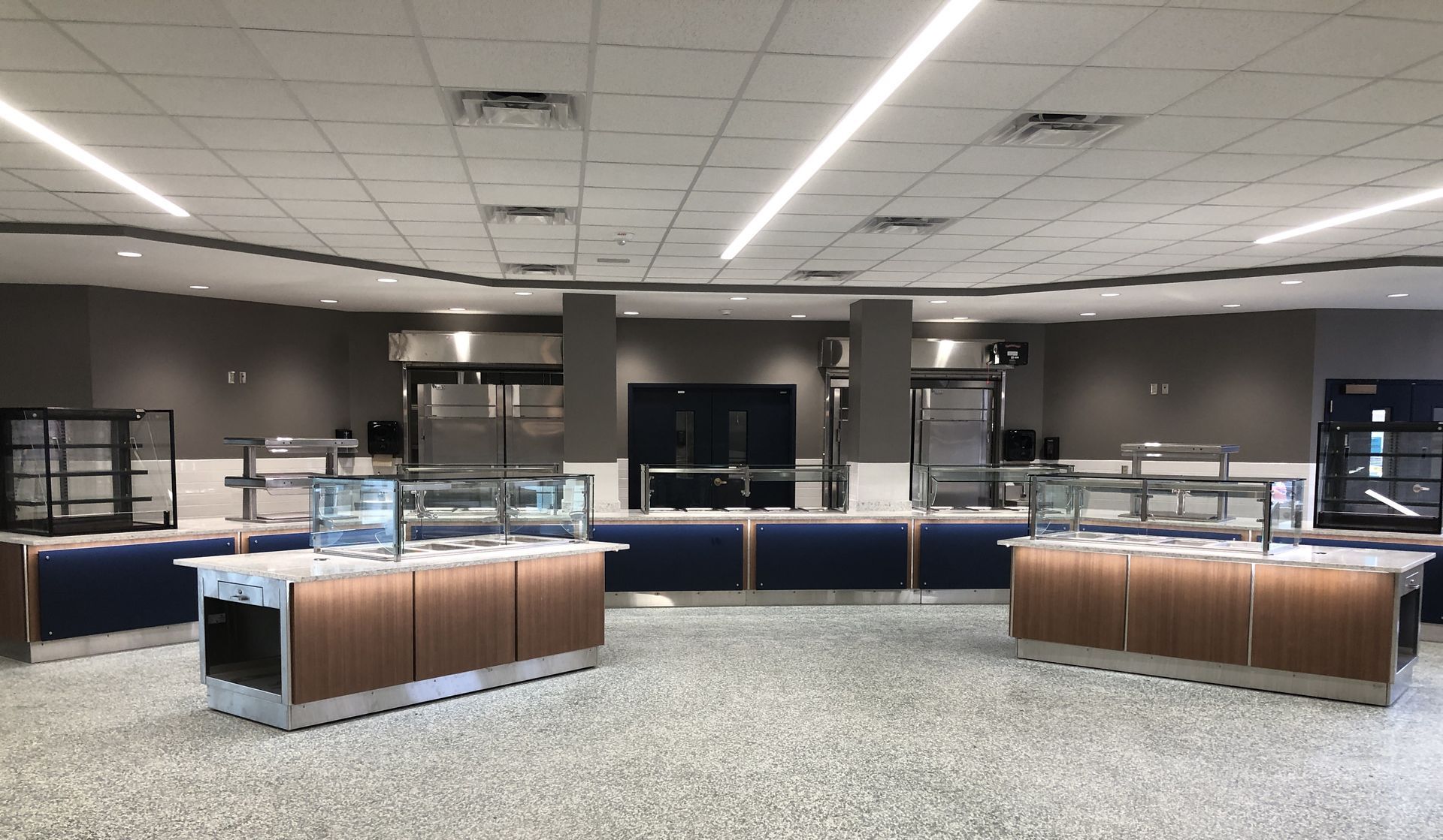A modern, empty cafeteria serving area featuring food stations with glass sneeze guards and blue and wood cabinetry.