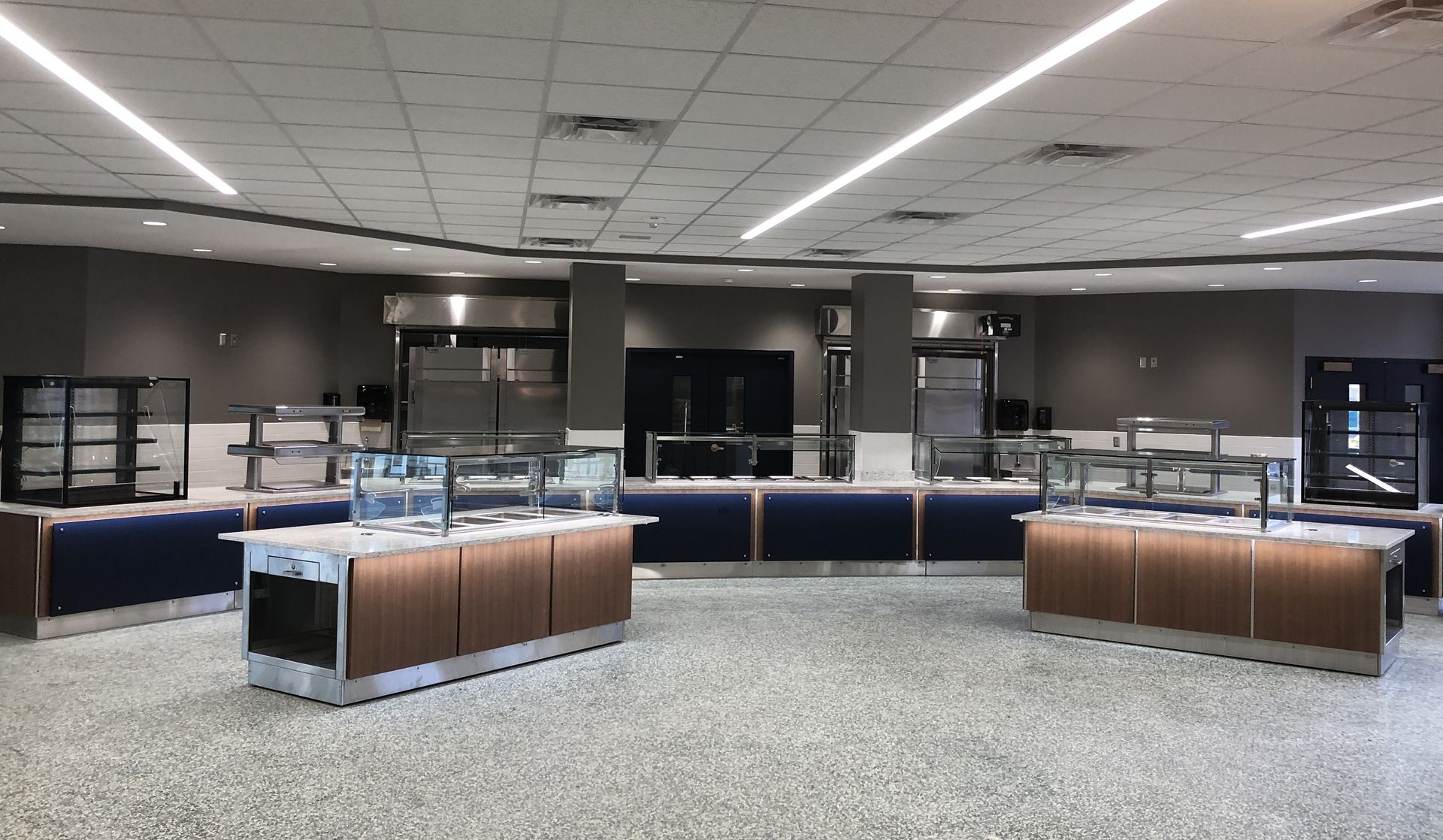 An empty cafeteria serving area with modern stainless steel buffet stations, dark blue accents, and bright lighting.
