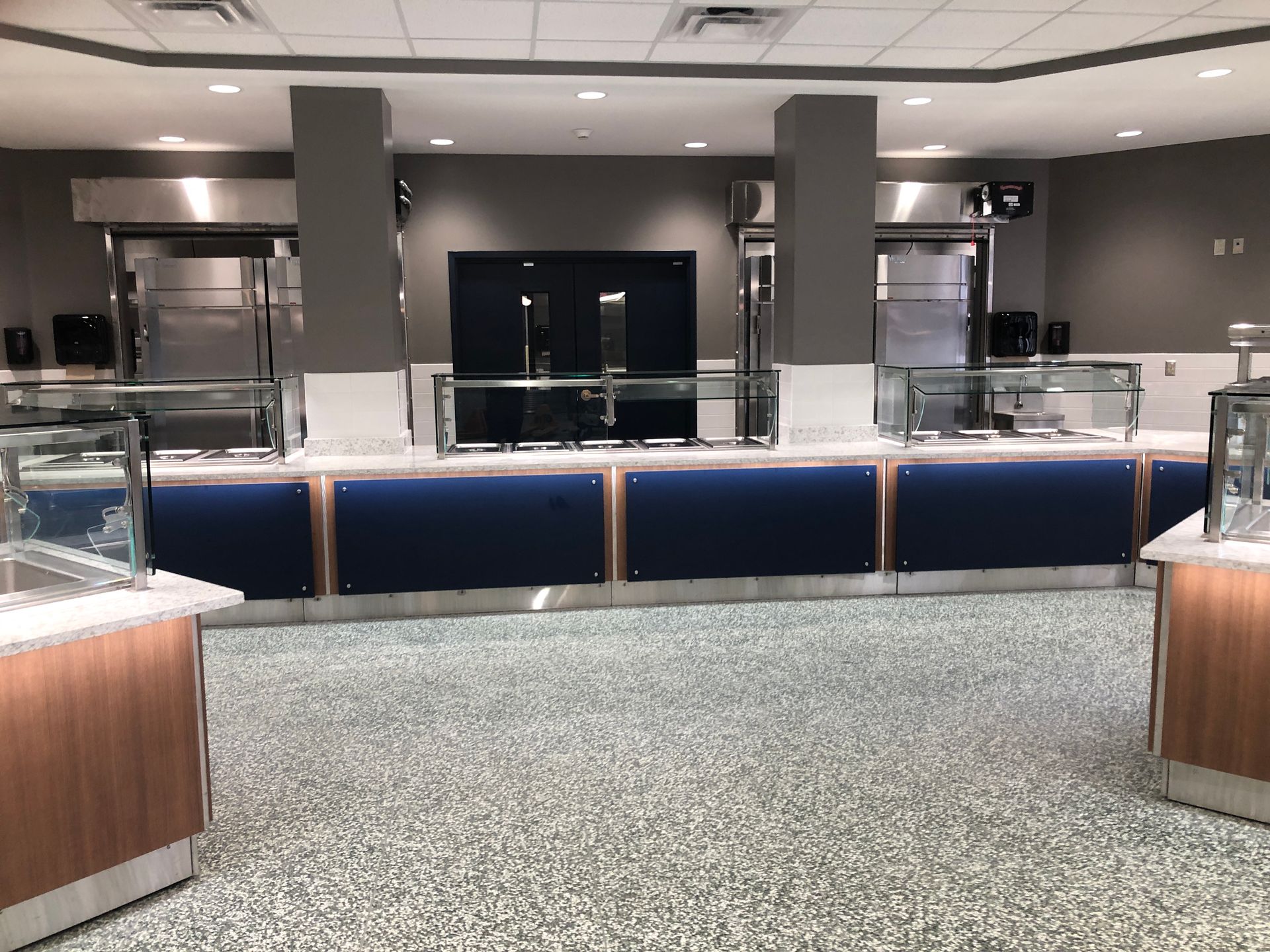 A modern, empty food service station with blue panels, stainless steel equipment, and speckled flooring.