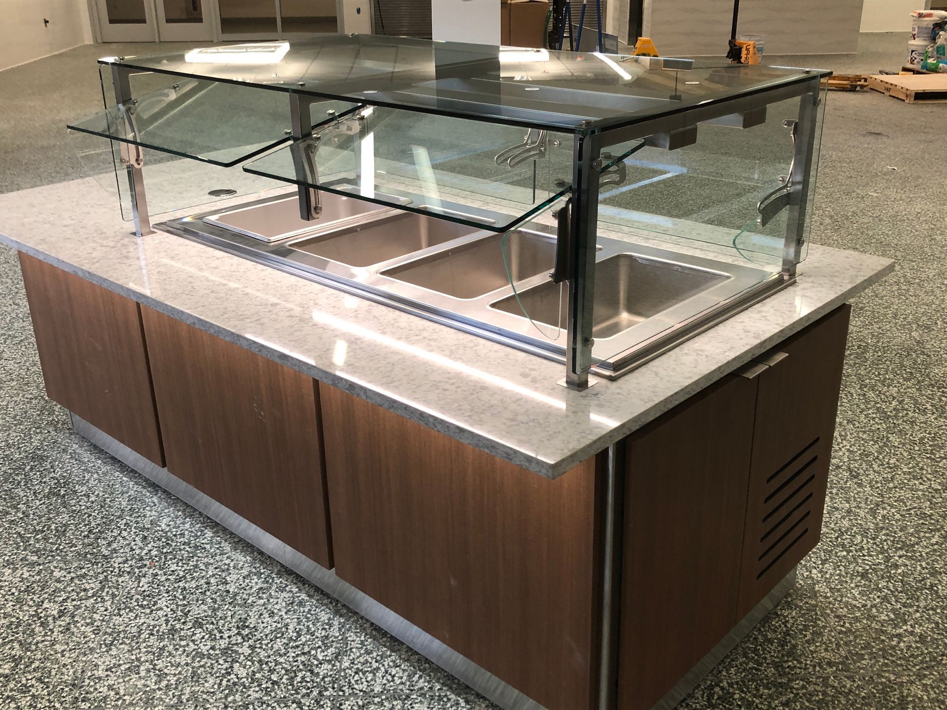 A wood-paneled food service buffet counter with a glass sneeze guard and three metal food warming wells.