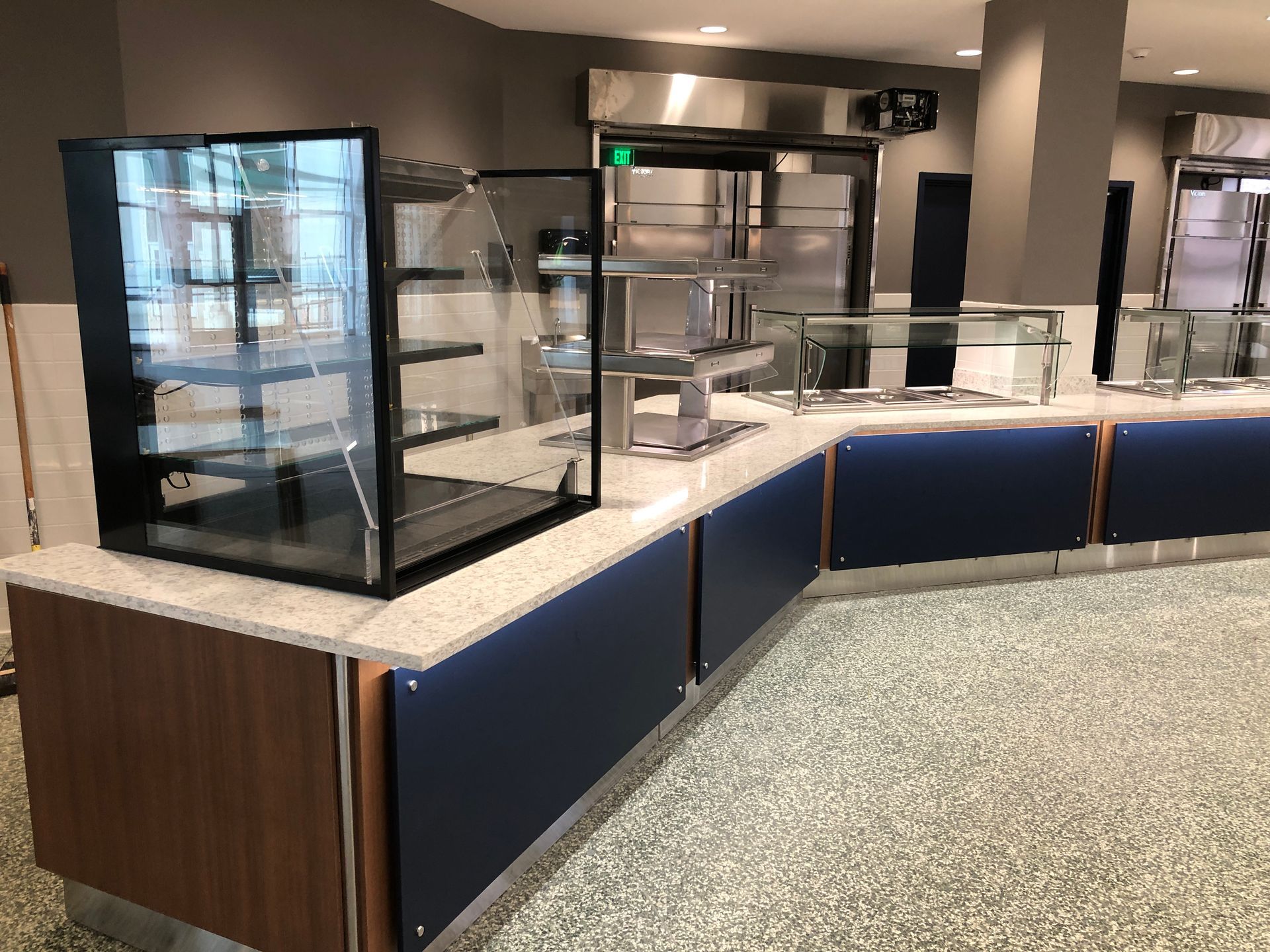 A modern cafeteria serving station with blue panels, a light speckled countertop, and glass display cases.