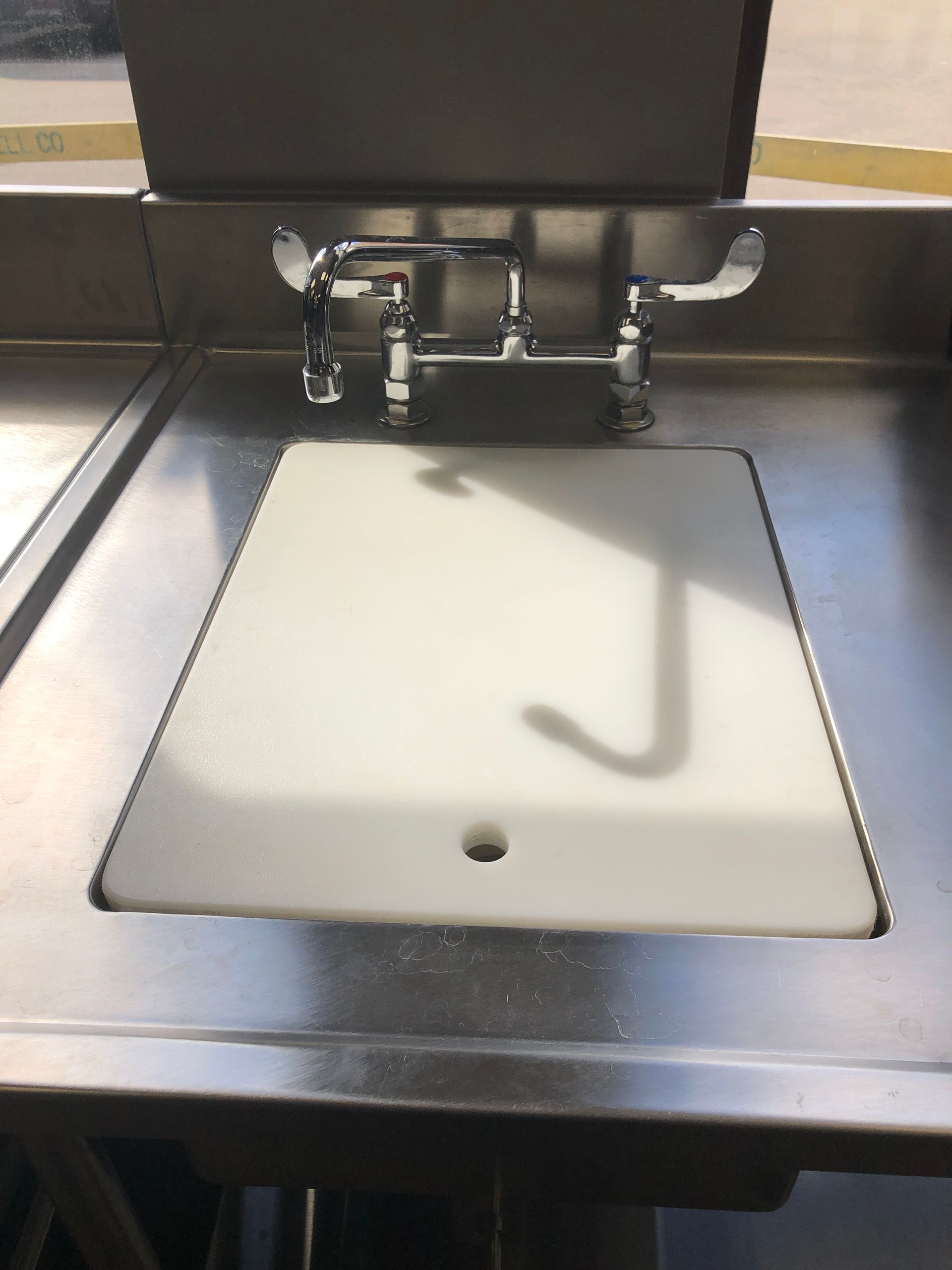 A stainless steel sink with a chrome faucet and a white rectangular cutting board covering the basin.