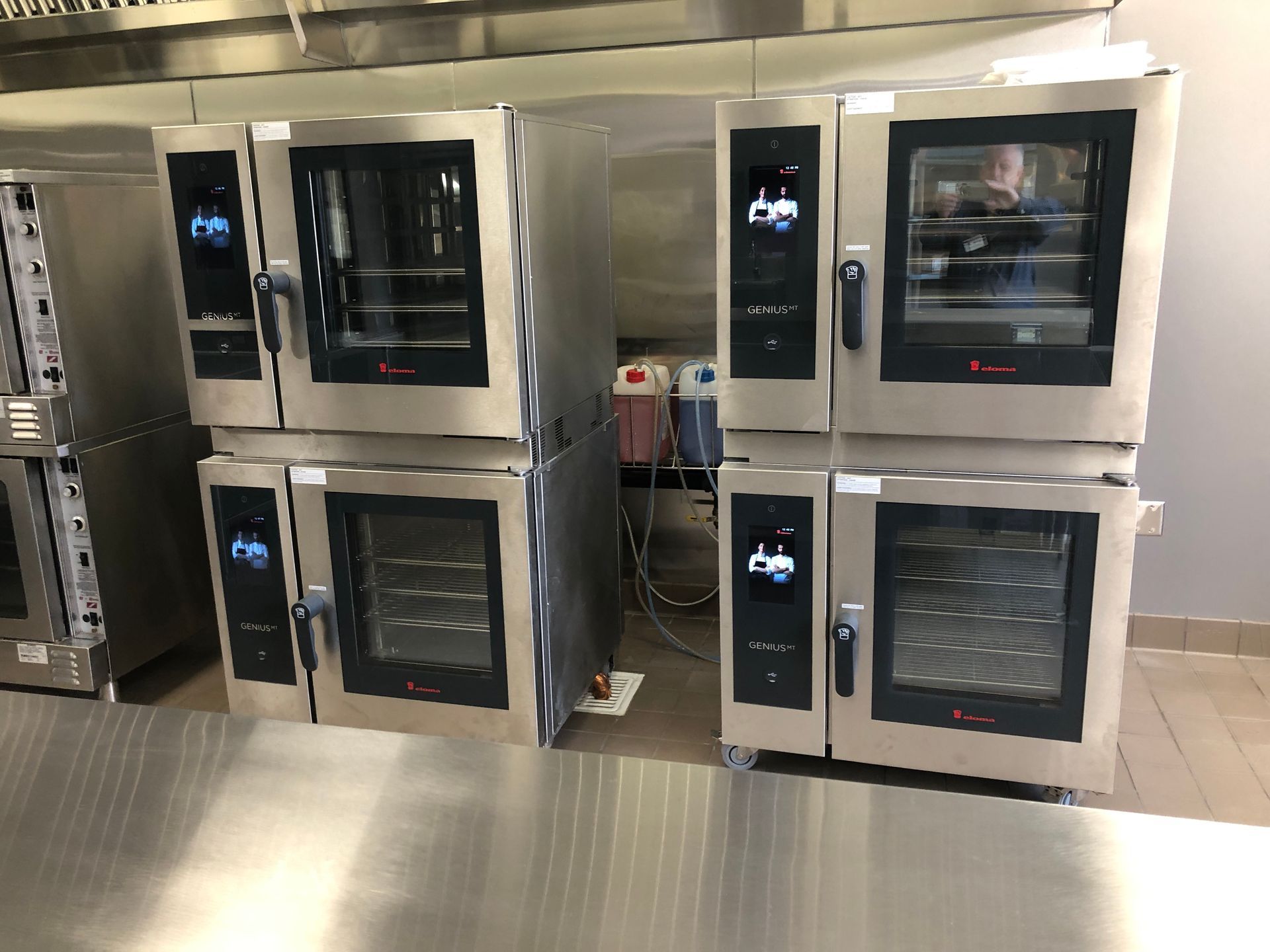 Two stacks of stainless steel commercial combi ovens stand side-by-side in a professional kitchen.