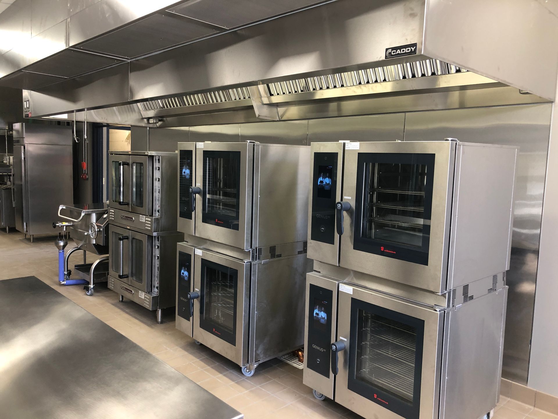 Three stacked commercial convection ovens in a stainless-steel commercial kitchen under a ventilation hood.