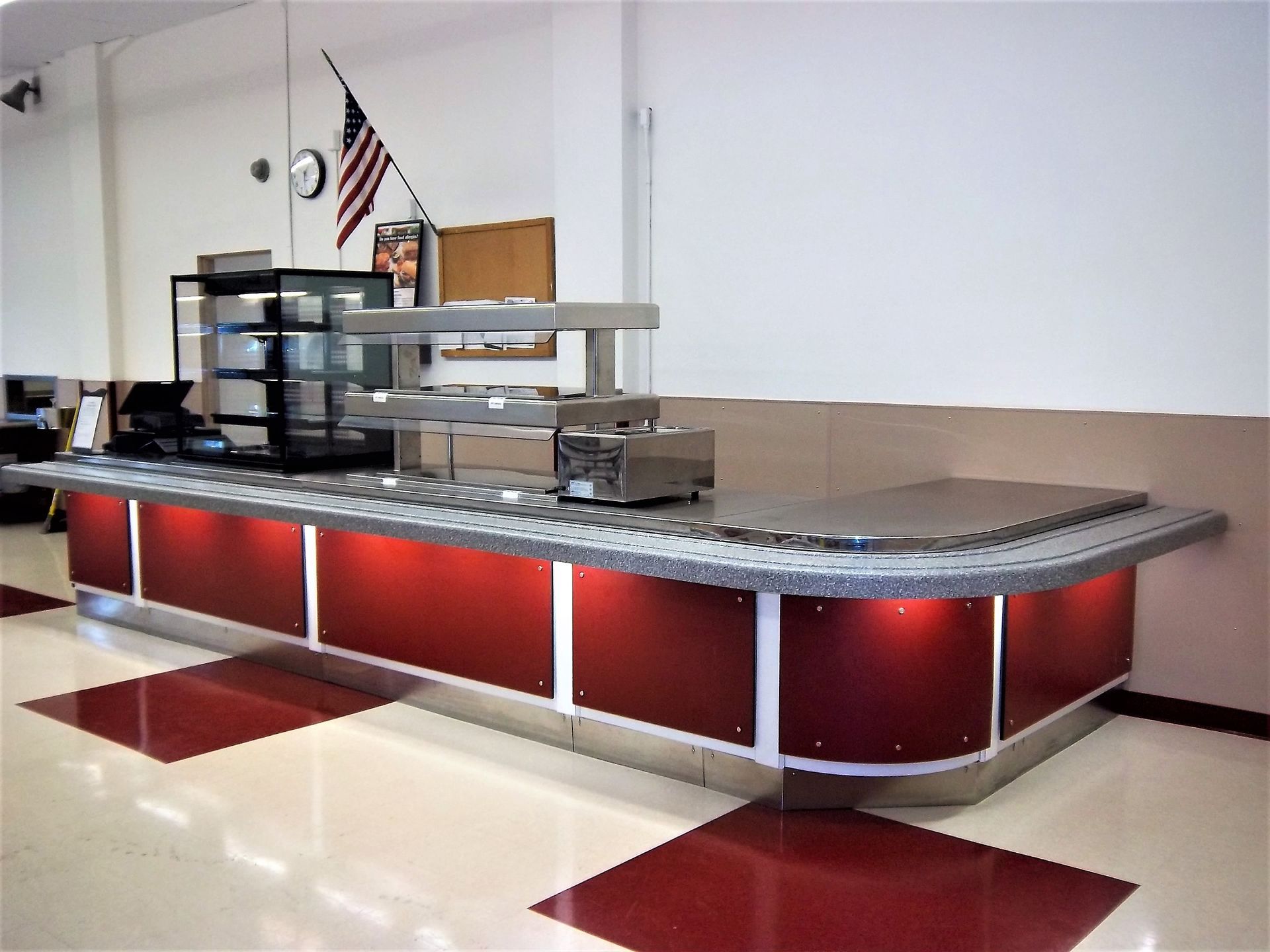 A modern food service counter with red panels and stainless steel fixtures, set in a brightly lit indoor space.
