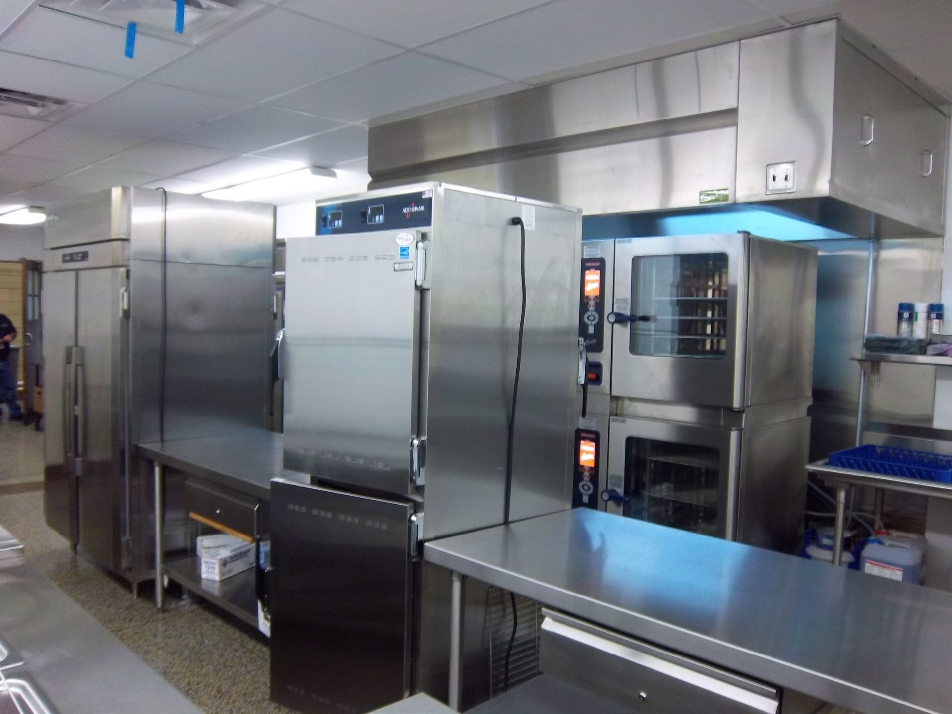 A commercial kitchen featuring stainless steel appliances, including a refrigerator, ovens, and a metal prep table.