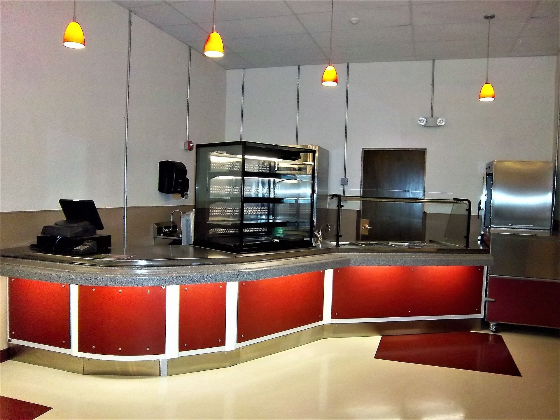 A food service counter with a granite top, red panels, illuminated display case, and pendant lighting.