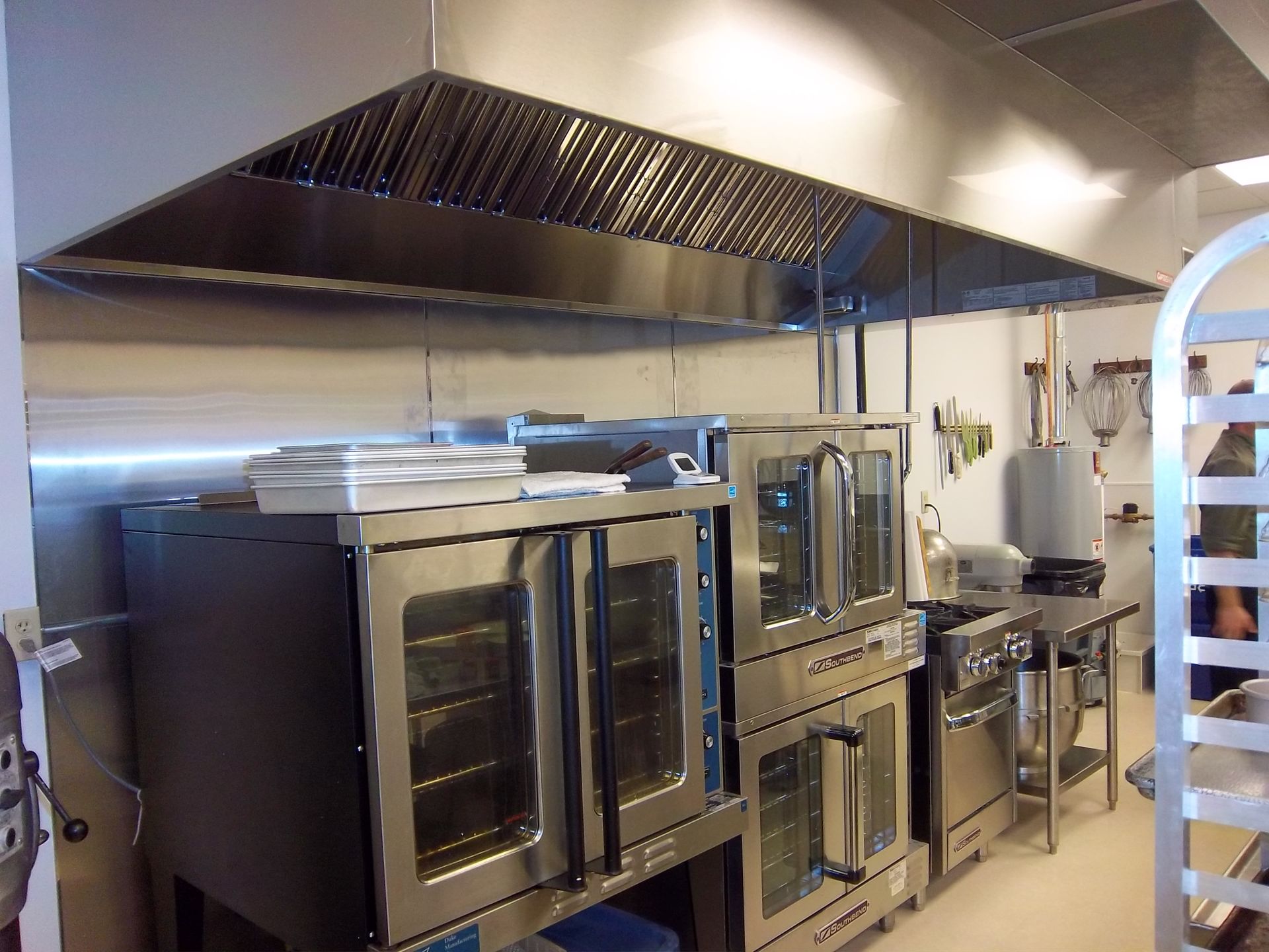 Commercial kitchen with stainless steel convection ovens and a large ventilation hood above.