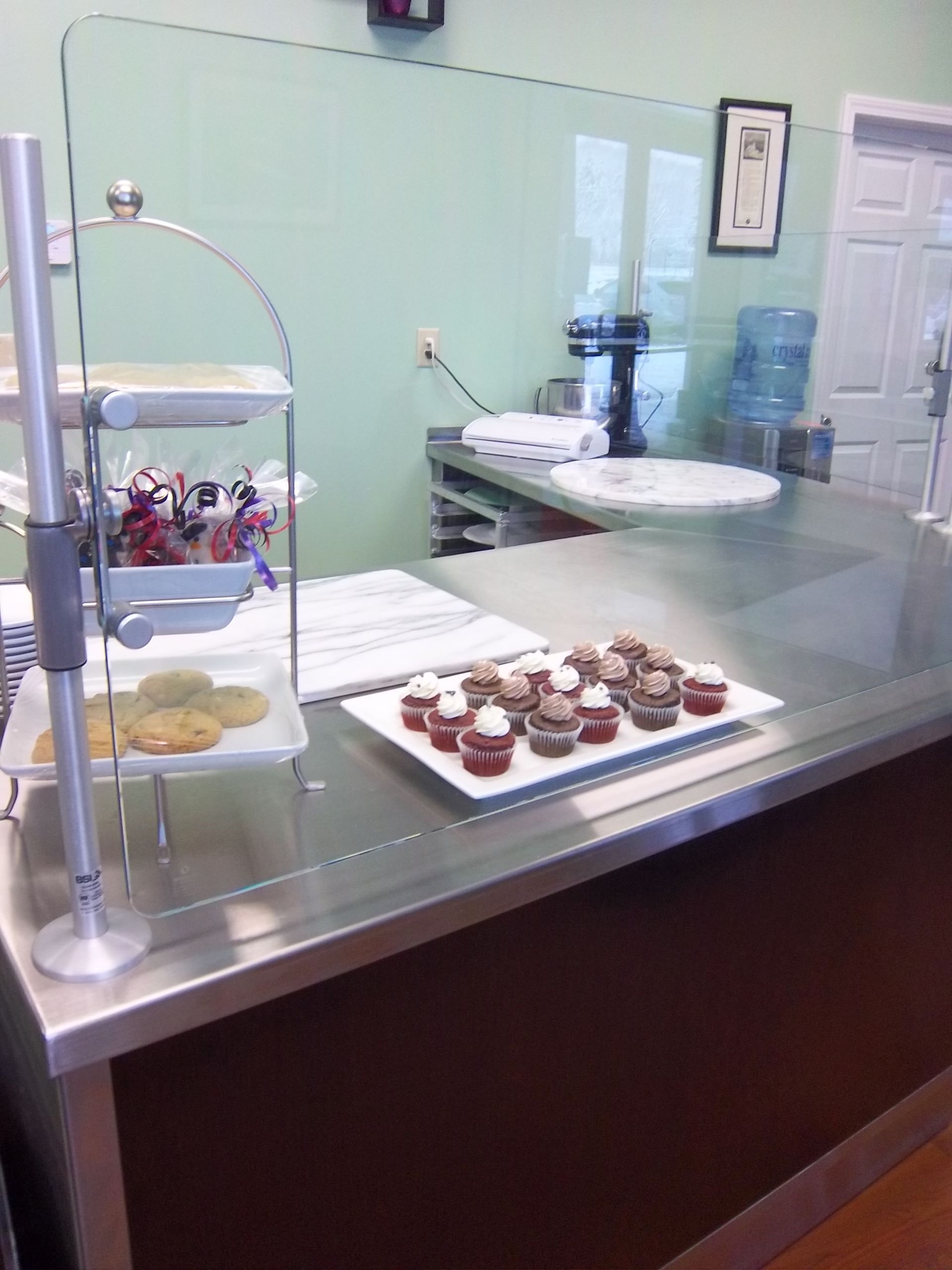 A counter in a bakery displays a tiered tray of cookies and a white rectangular platter of frosted mini cupcakes.