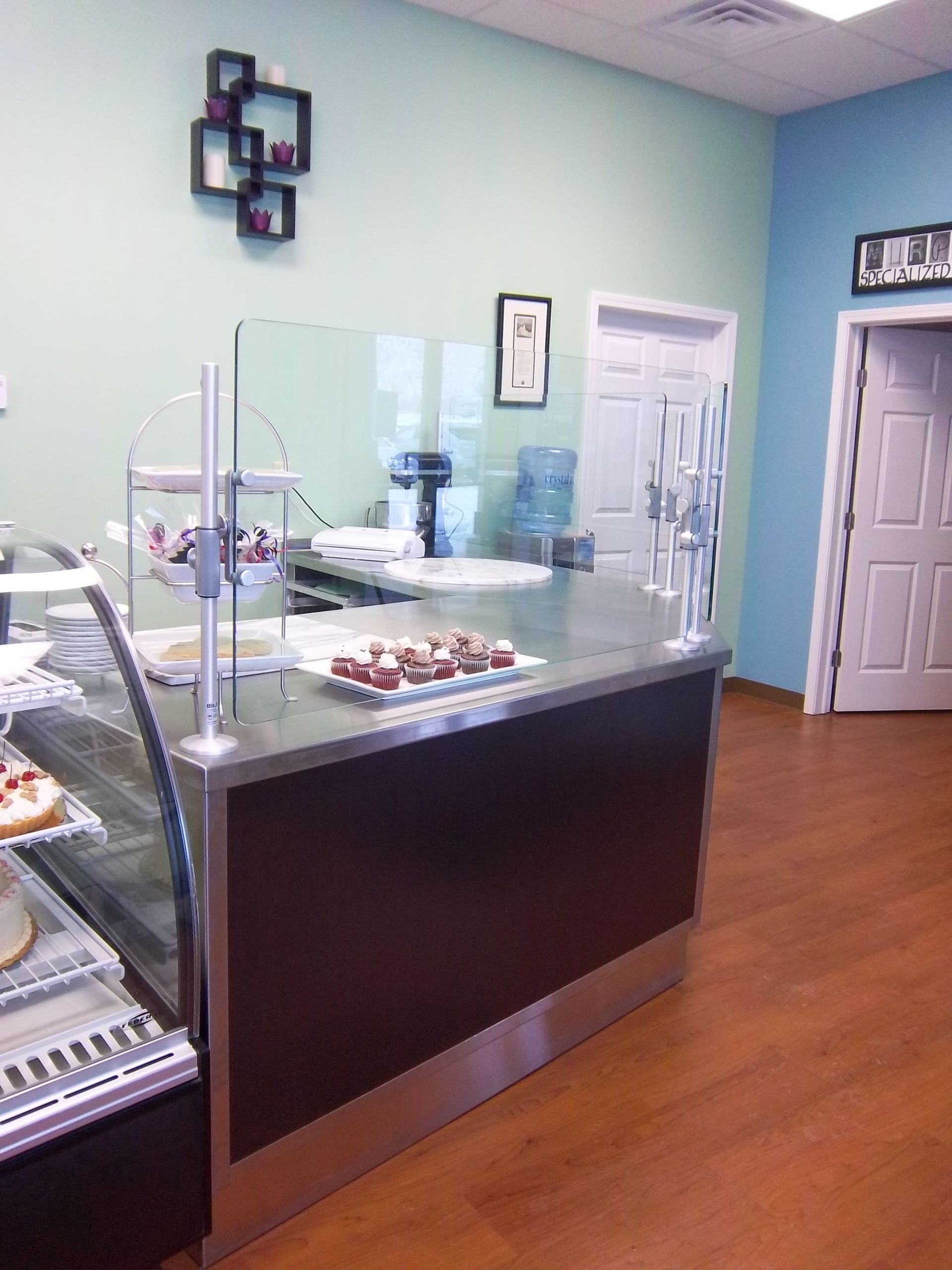 A bakery service counter with glass displays, pastries, and modern decor against light blue and mint walls.
