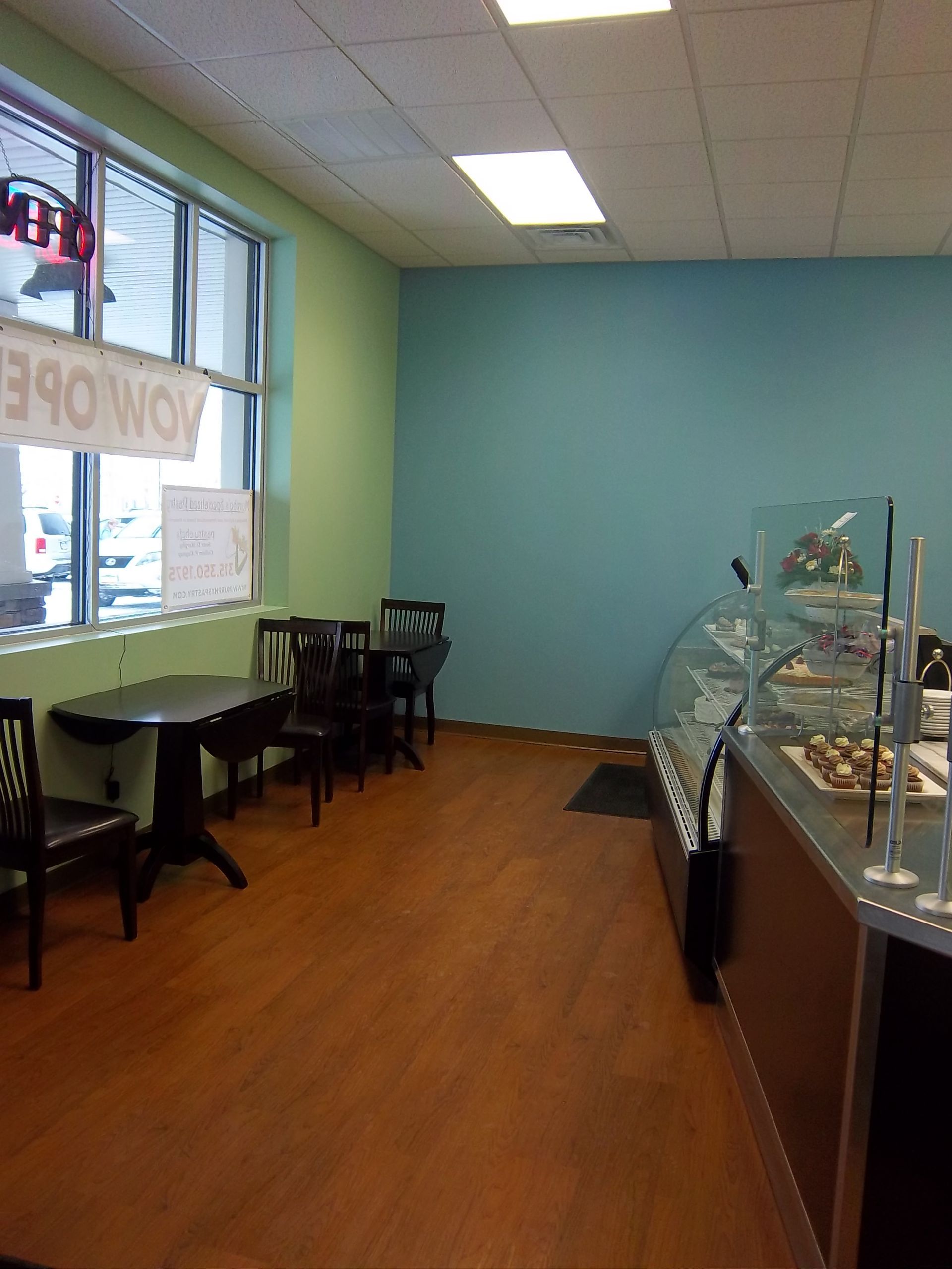 A small cafe interior with a turquoise wall, light green wall, wooden floors, tables with chairs, and a pastry display.