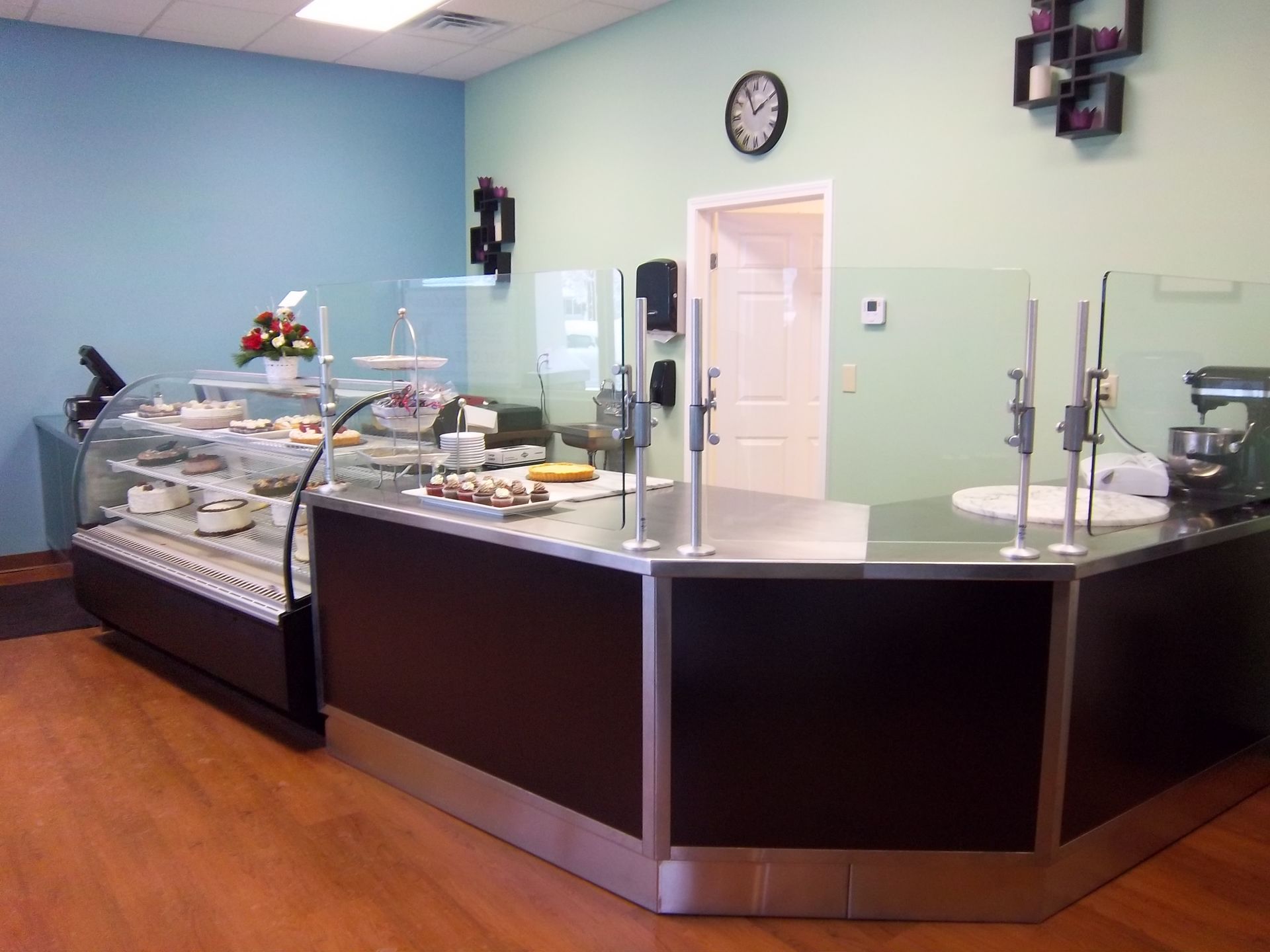 A bakery counter with a glass display case full of pastries, a stainless steel work surface, and light-colored walls.