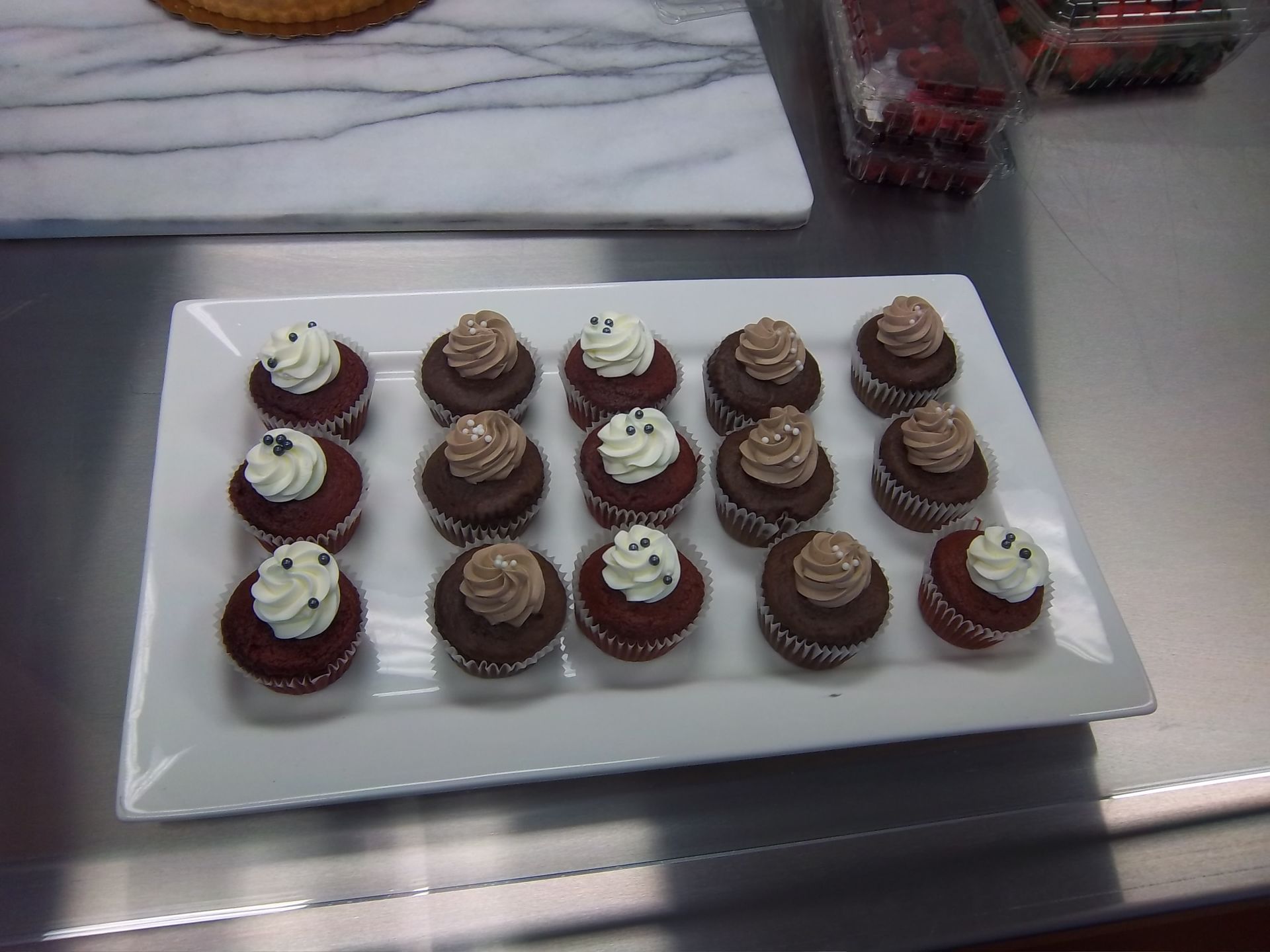 A white rectangular platter holds 15 small chocolate and red velvet cupcakes with vanilla and chocolate frosting.