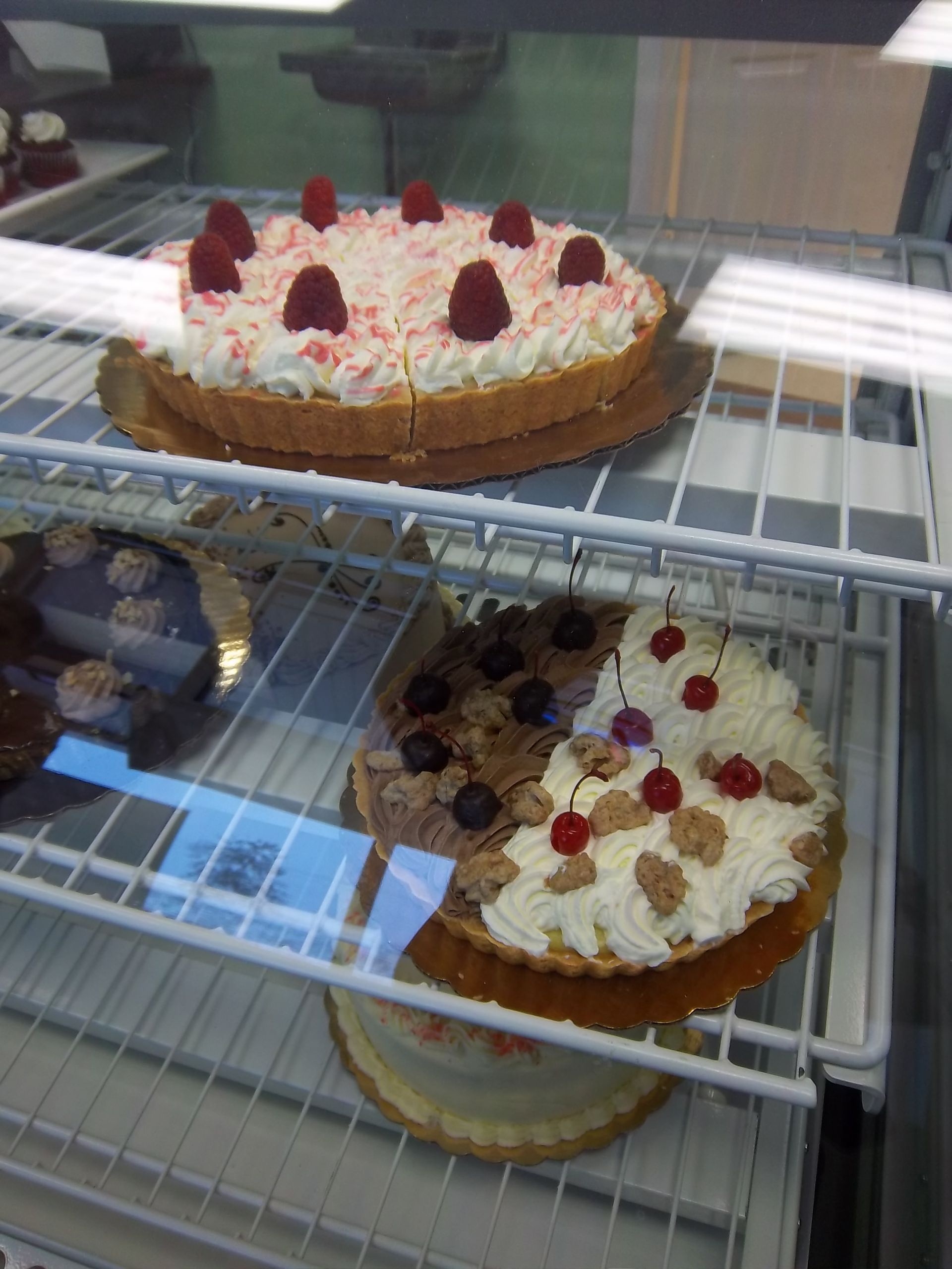 Display case with tarts: one with raspberries and white frosting on top, another with cherries and cream on bottom shelf.