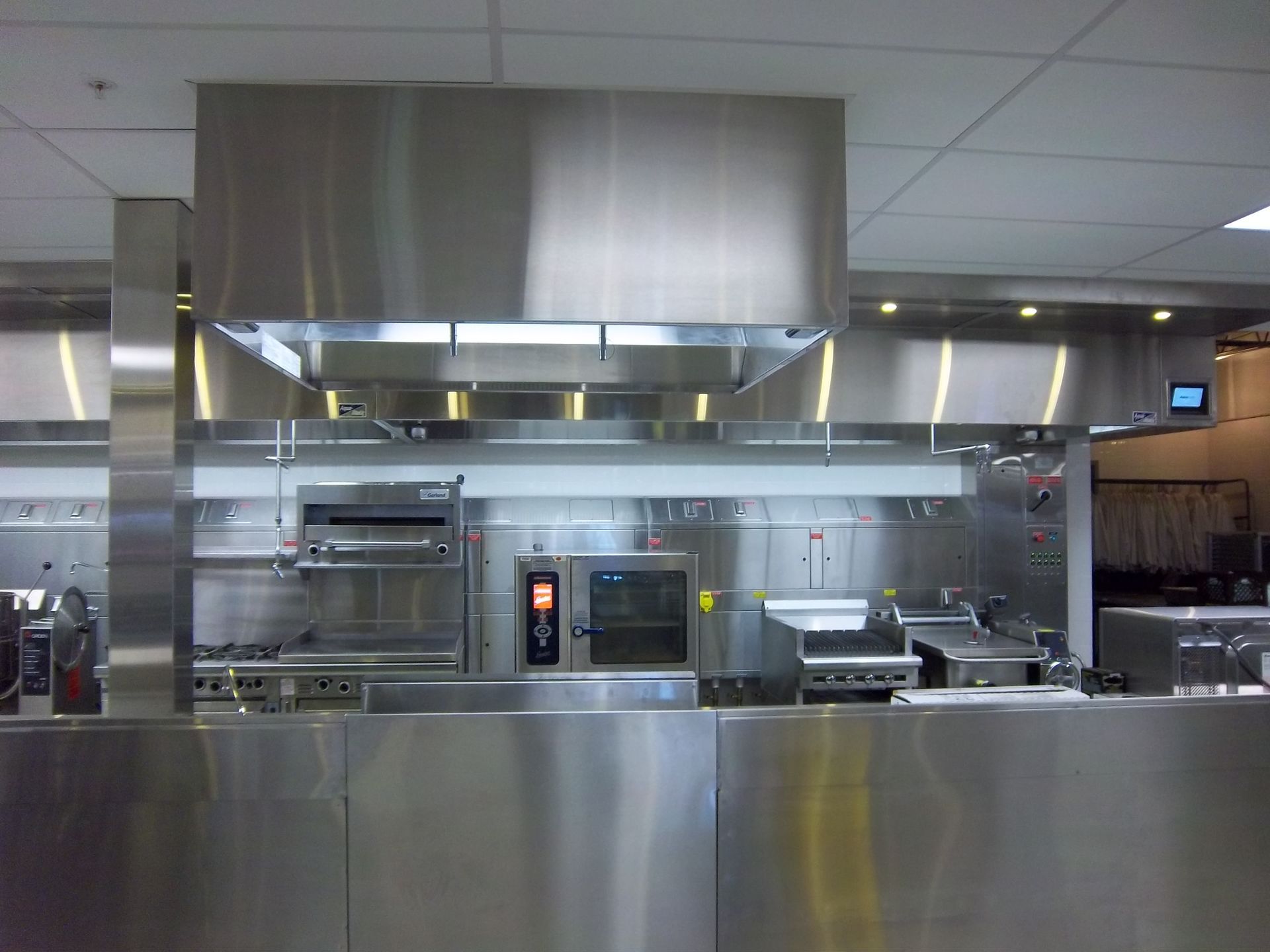 A modern professional stainless-steel kitchen with a large vent hood over cooking appliances and prep counters.