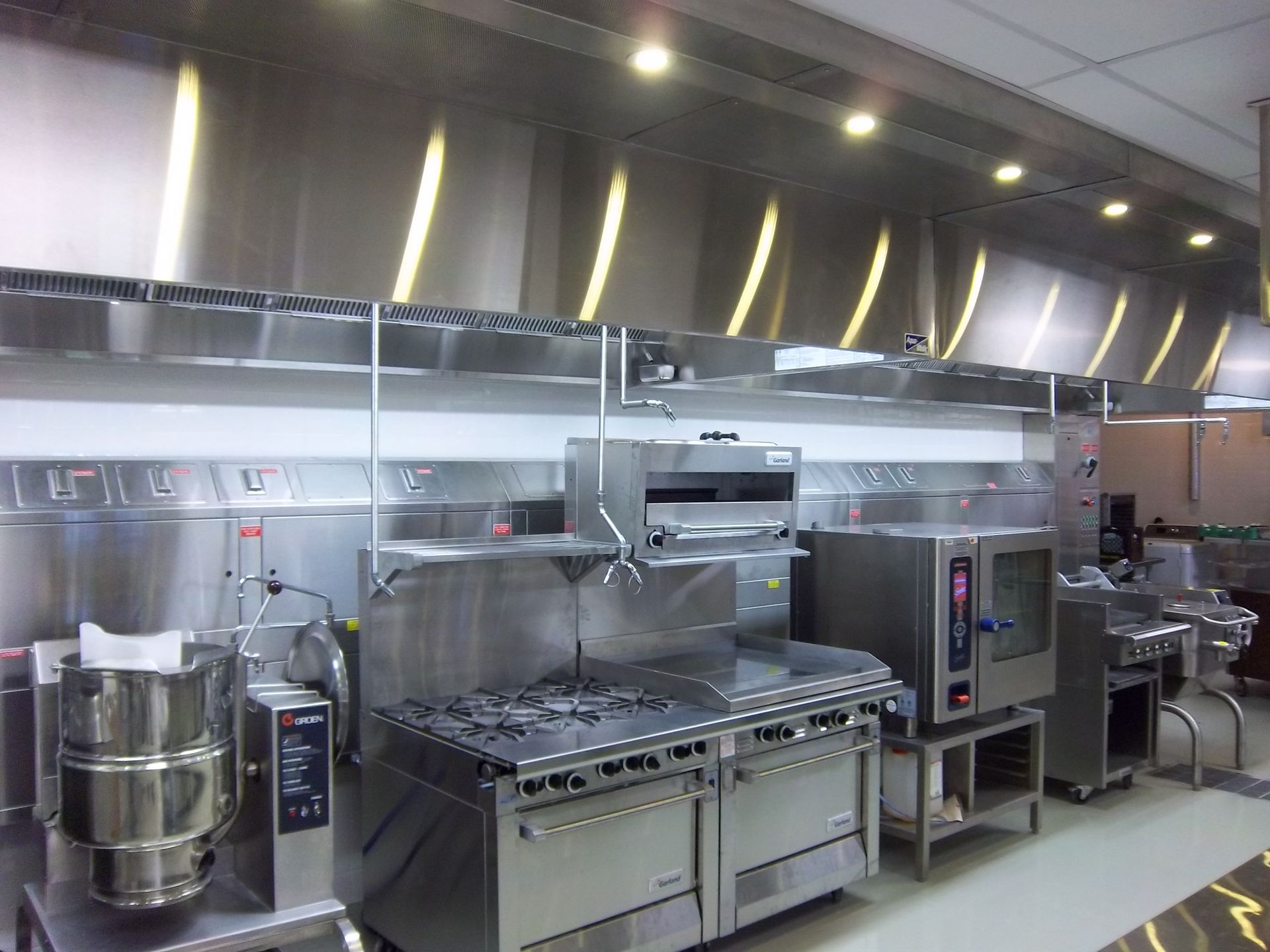 A professional commercial kitchen featuring stainless steel stoves, a food processor, and an industrial vent hood.