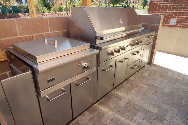 Stainless steel outdoor kitchen grill station with a flat-top griddle on a stone patio.