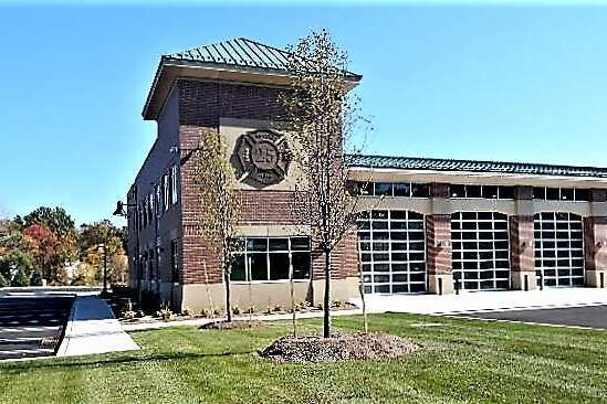 A modern brick fire station with large glass garage doors and a fire department emblem on the tower under a blue sky.