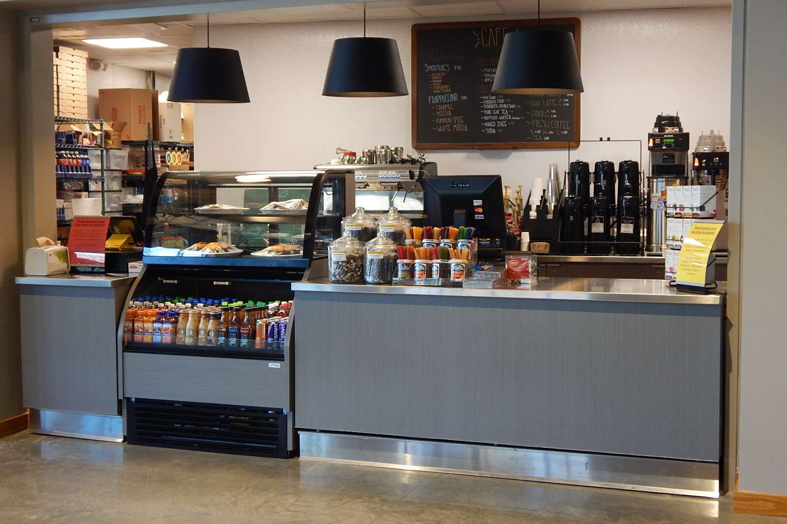 A clean, modern café counter featuring glass display cases, a menu board on the wall, and three large hanging lights.