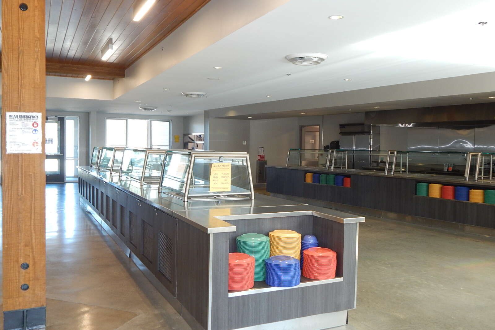 A cafeteria buffet line with stainless steel counters and stacks of colorful plates in the foreground.