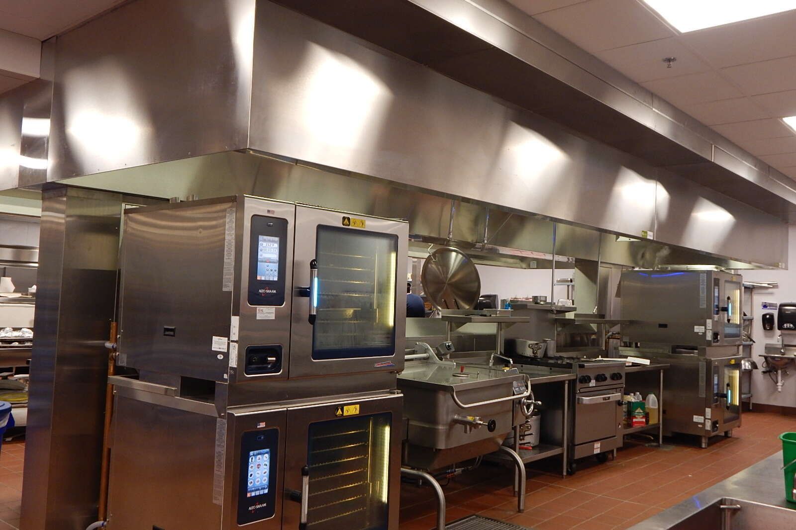 Professional stainless steel kitchen featuring stacked commercial ovens under a large ventilation hood.