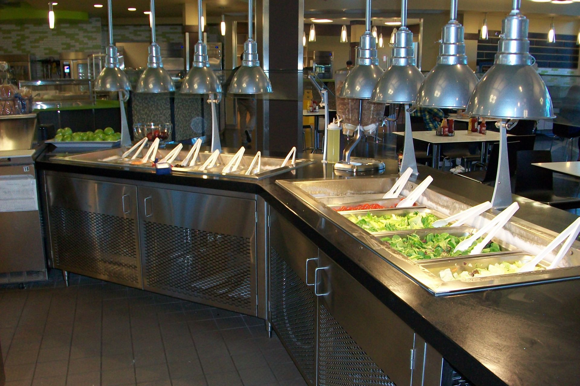 A stainless steel buffet salad bar with multiple hanging lights and serving tongs in a restaurant setting.