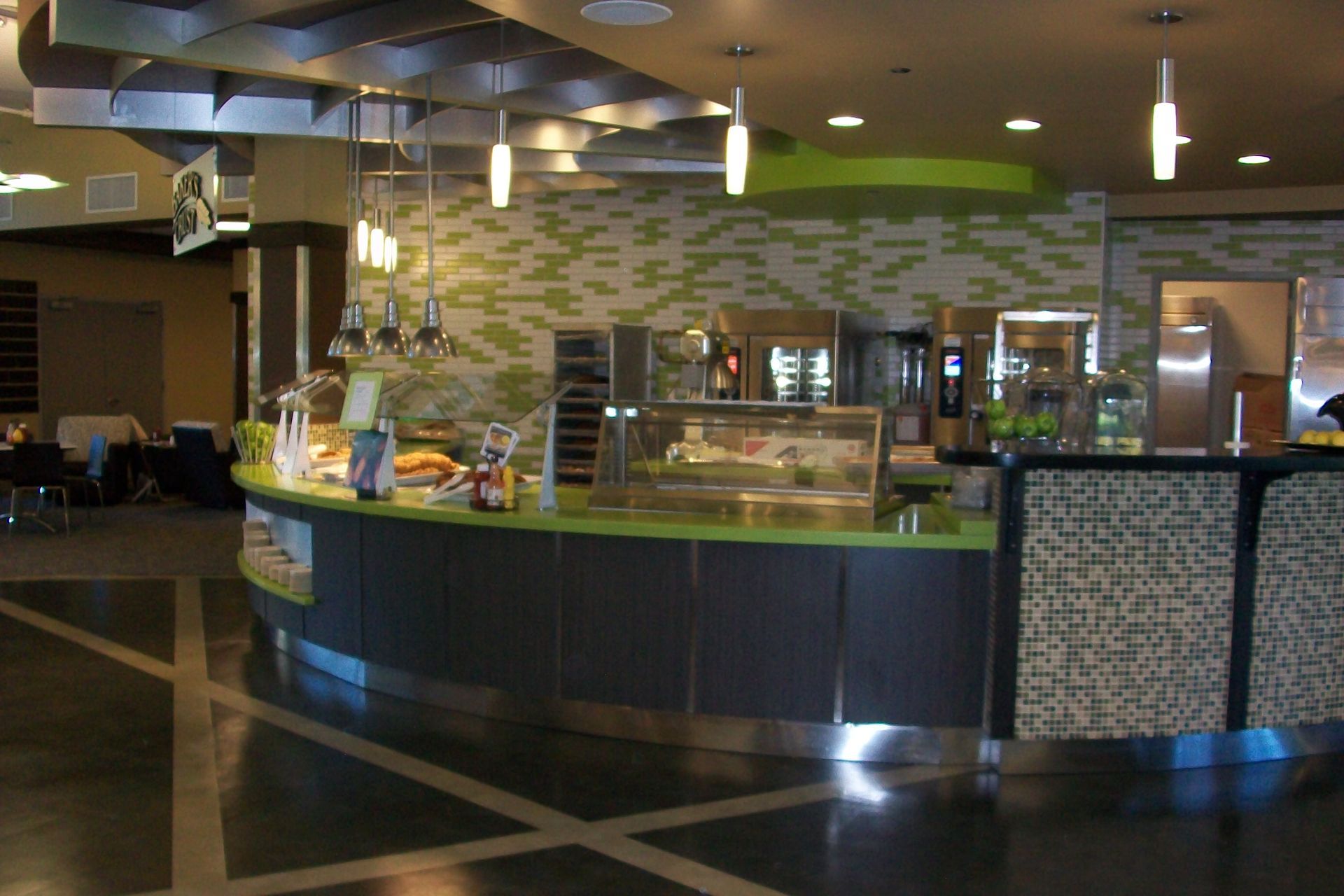 A modern, curved food service counter with green accents and hanging lights in a contemporary building interior.
