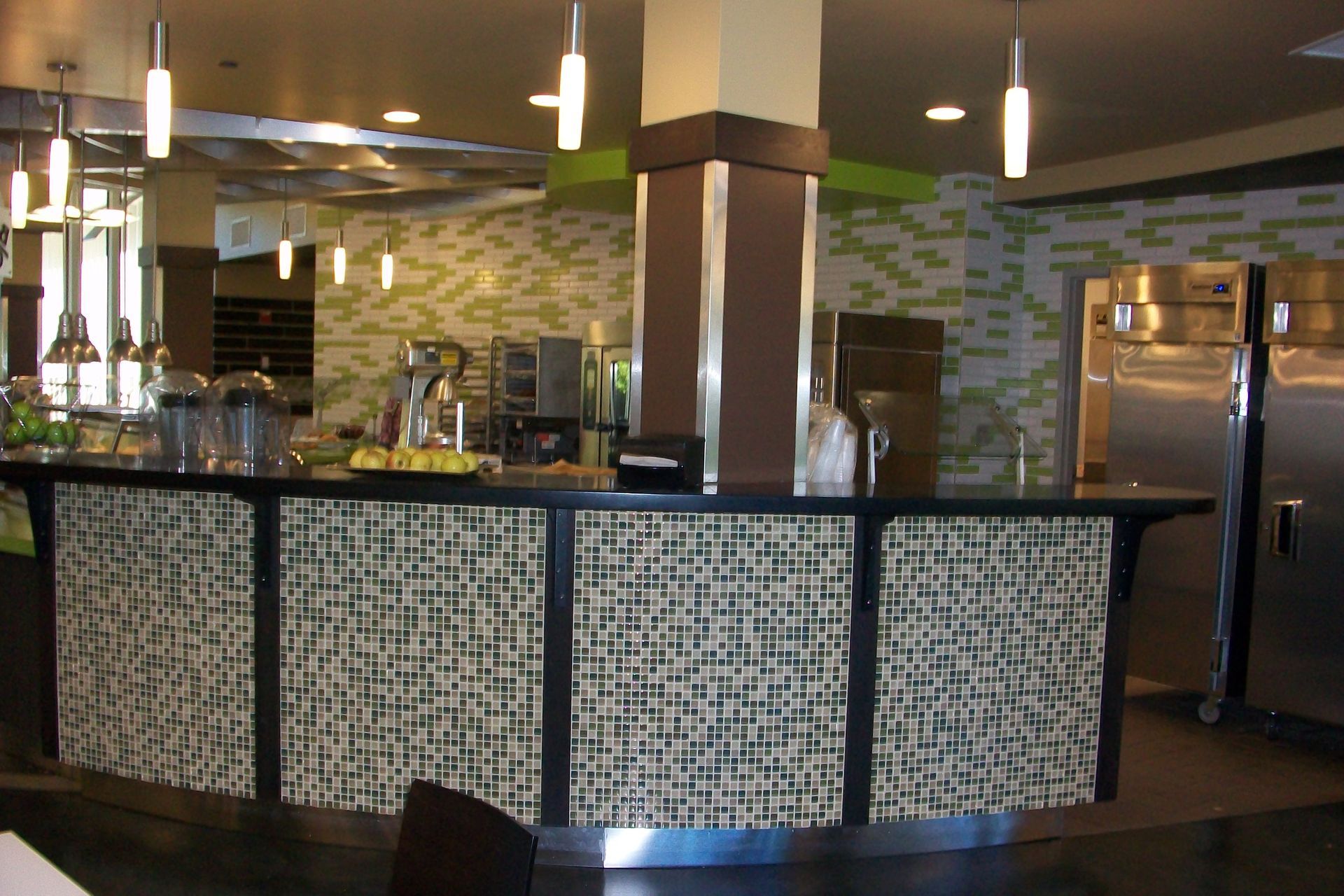 A service counter with a textured, patterned front panel, featuring pendant lighting and stainless steel appliances.