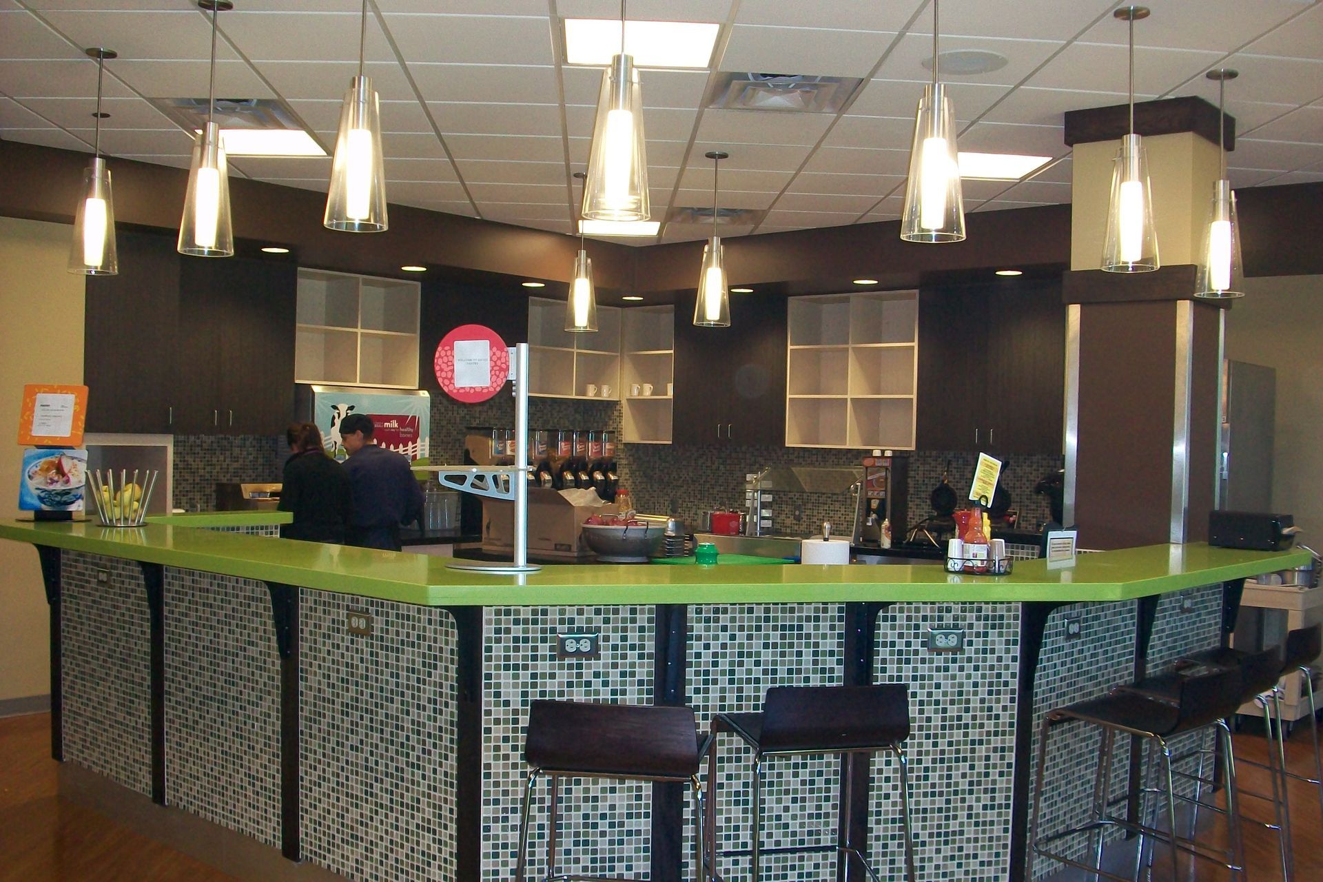 Modern breakroom with a lime green counter, dark cabinets, pendant lighting, and bar stools.