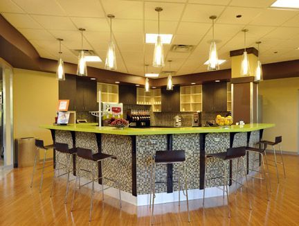 A curved lime green bar counter with patterned front panels, surrounded by dark high stools under hanging pendant lights.