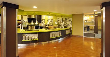 A buffet counter with green counters, brown wood accents, and light-colored flooring in a modern, well-lit dining area.