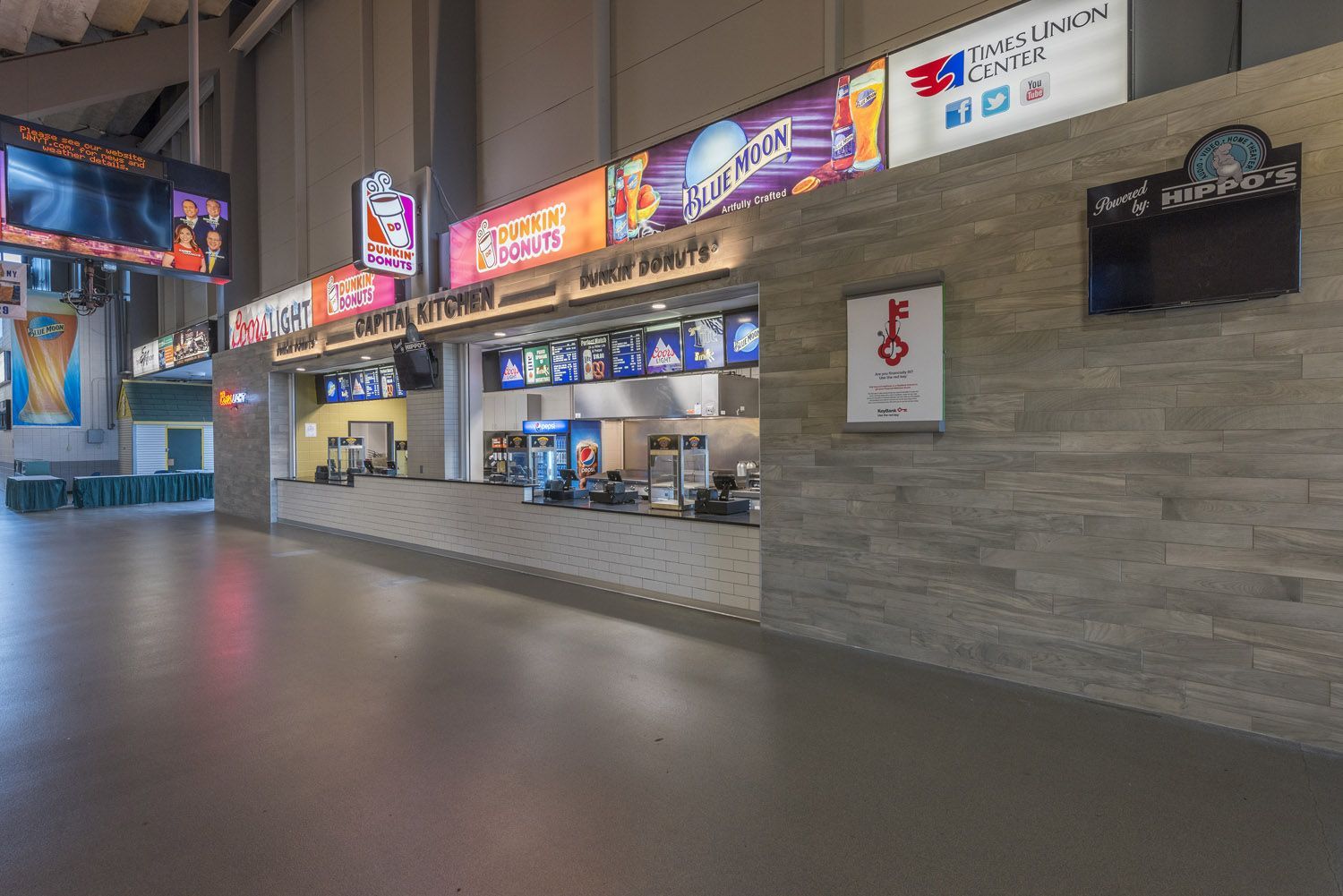 Concession stand in an arena concourse with stone-textured walls and illuminated brand signage above the service counter.