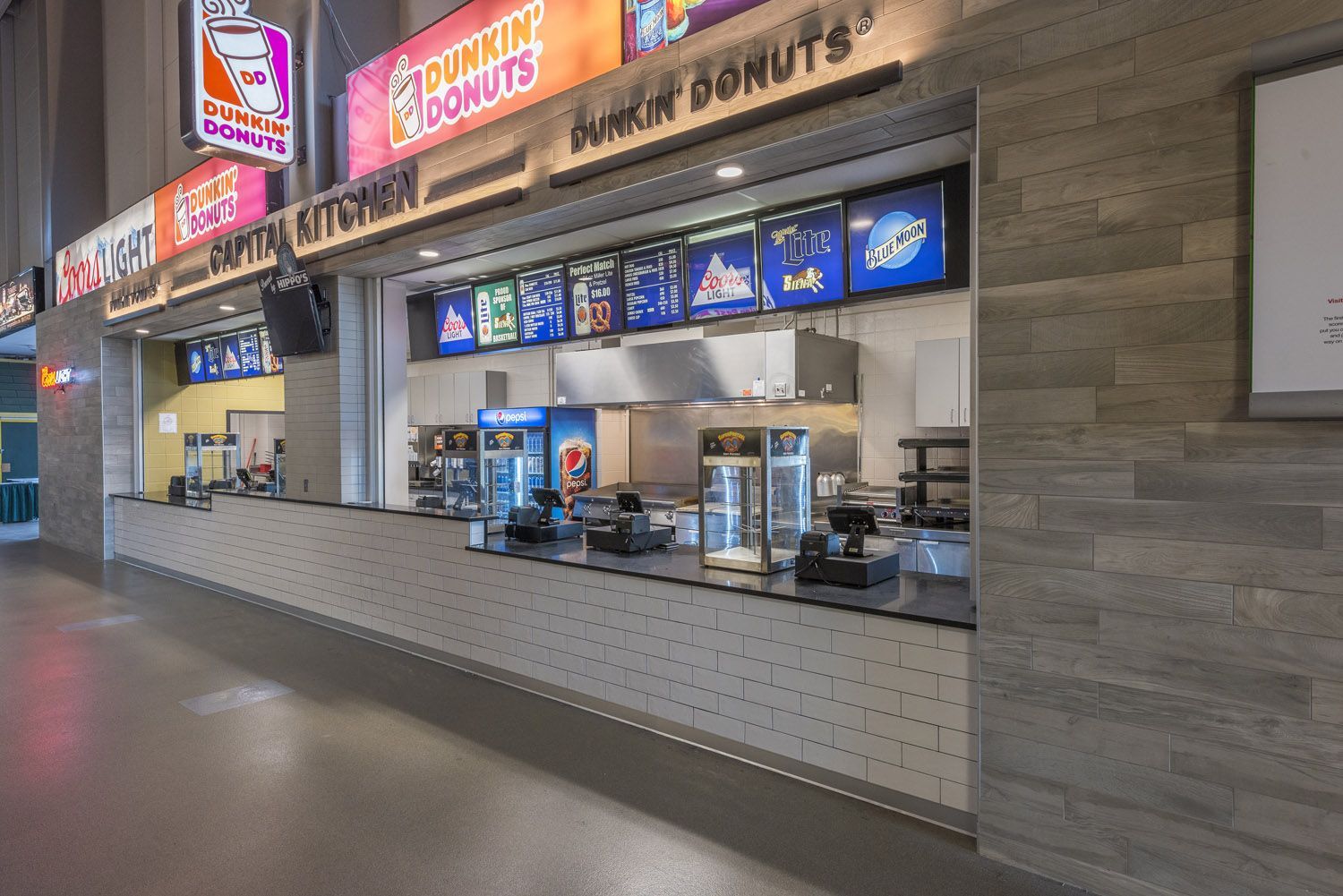 A modern Dunkin' Donuts concession stand inside a large building with stone-textured walls and a long serving counter.