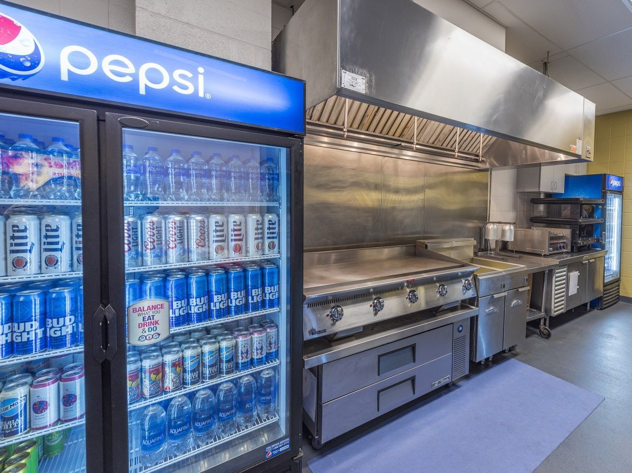 A commercial kitchen area featuring a Pepsi-branded glass-door refrigerator filled with beverages next to a stainless grill.