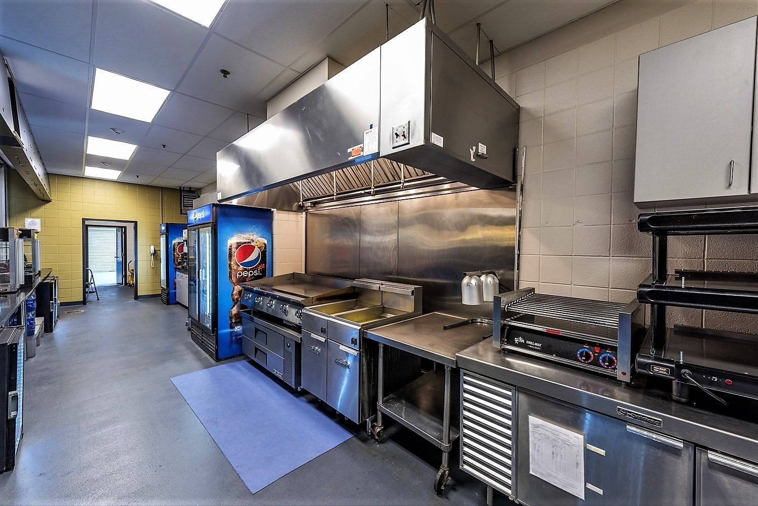 A commercial kitchen featuring stainless steel appliances, a large exhaust hood, a food prep area, and refrigeration units.