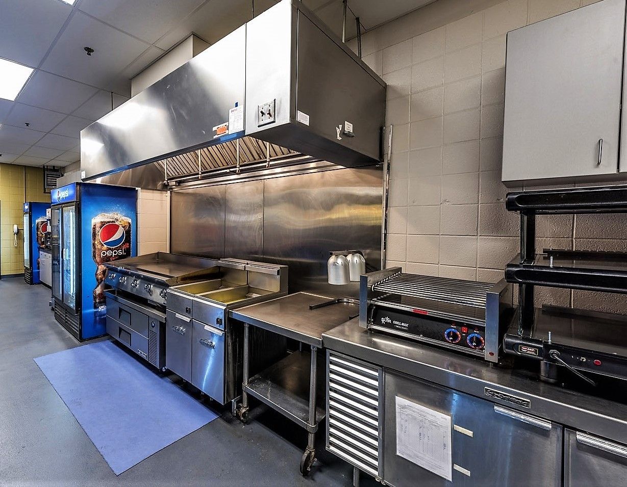 Commercial kitchen featuring stainless steel appliances, a range hood, and a refrigerator against a white brick wall.