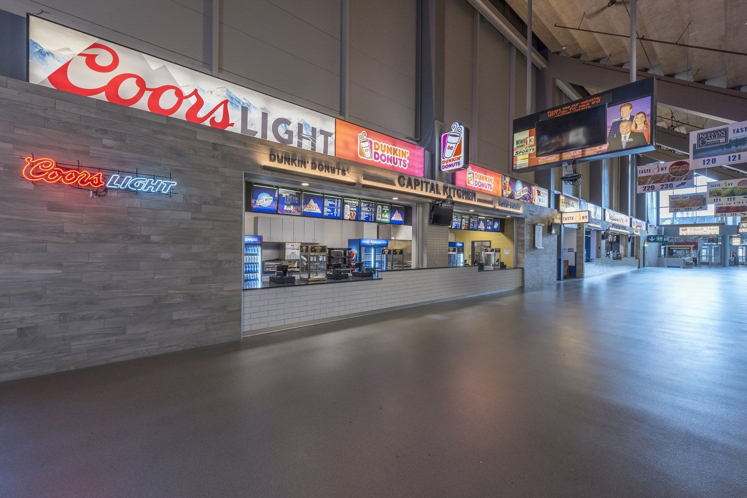 A concession stand inside an arena, featuring Coors Light signage, menu boards, and a stone wall exterior.