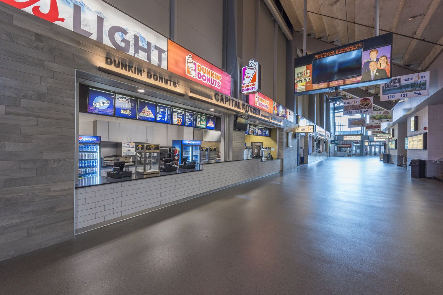 A brightly lit, empty stadium concourse featuring a Bud Light and Dunkin’ concession stand with a grey tiled floor.