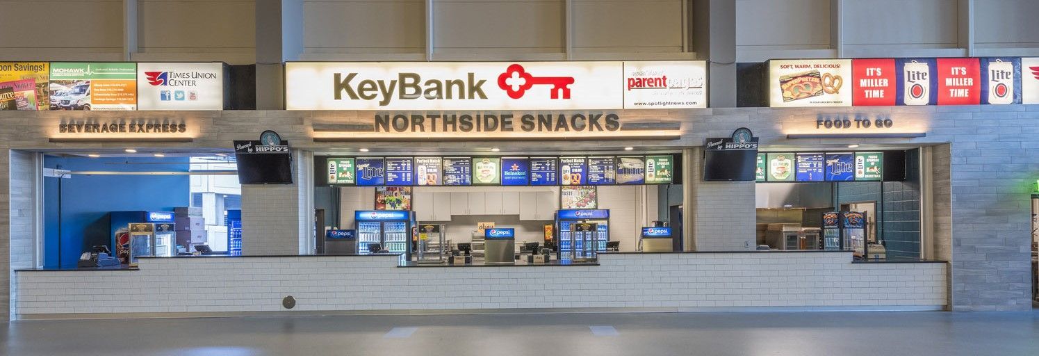 A wide, brightly lit concession stand in a stadium with KeyBank branding, multiple menus, and serving counters.