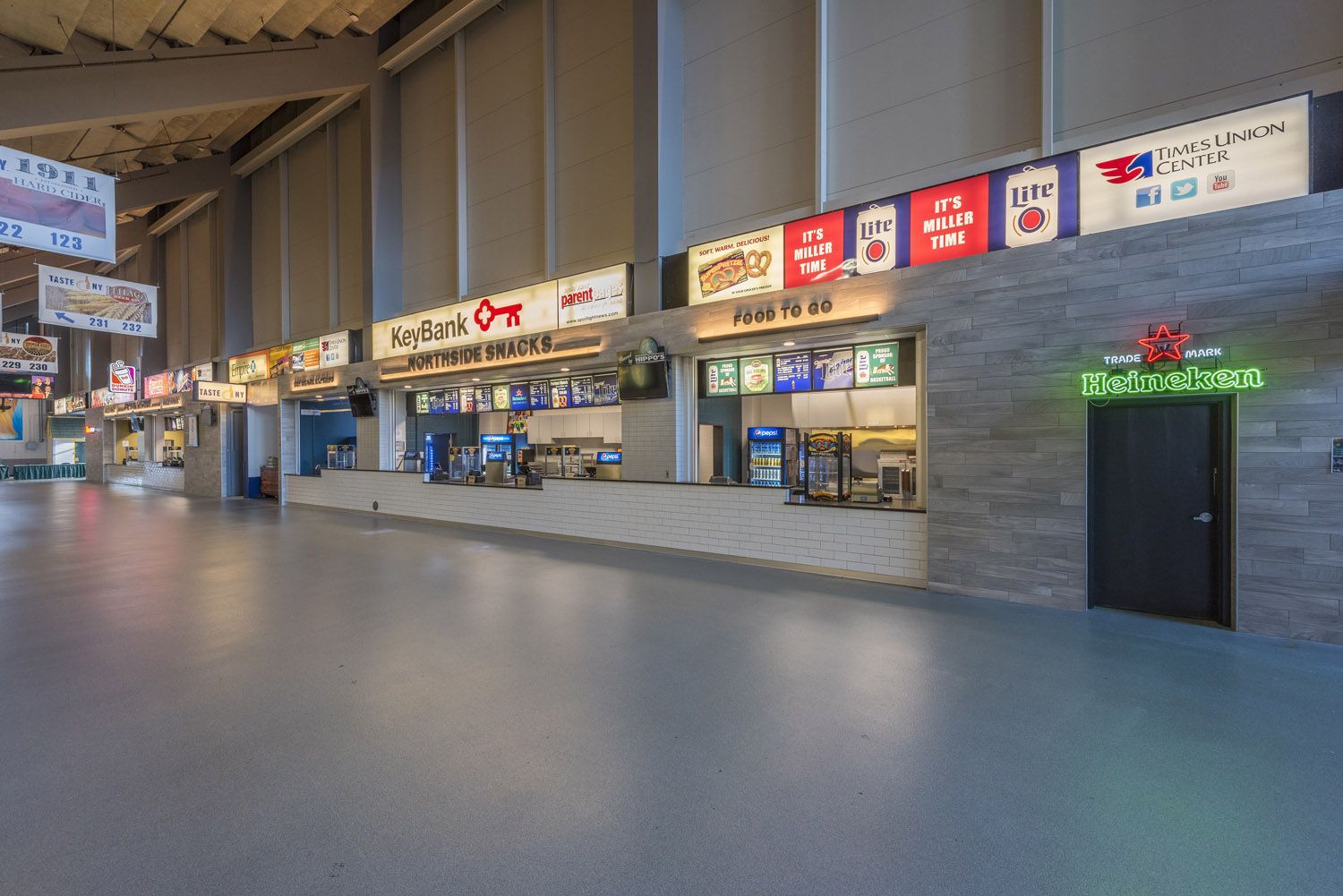 An empty stadium concourse featuring a long row of food concession stands with colorful signage and modern lighting.