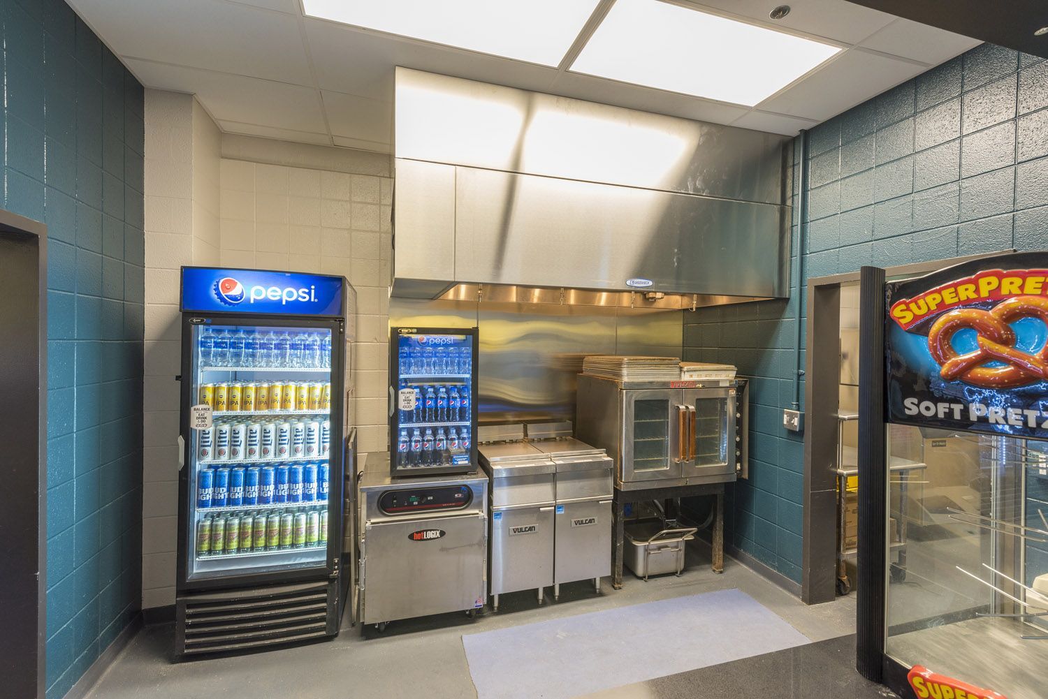 A concession stand featuring a glass-door Pepsi refrigerator, a stainless steel oven and prep area, and a pretzel warmer.