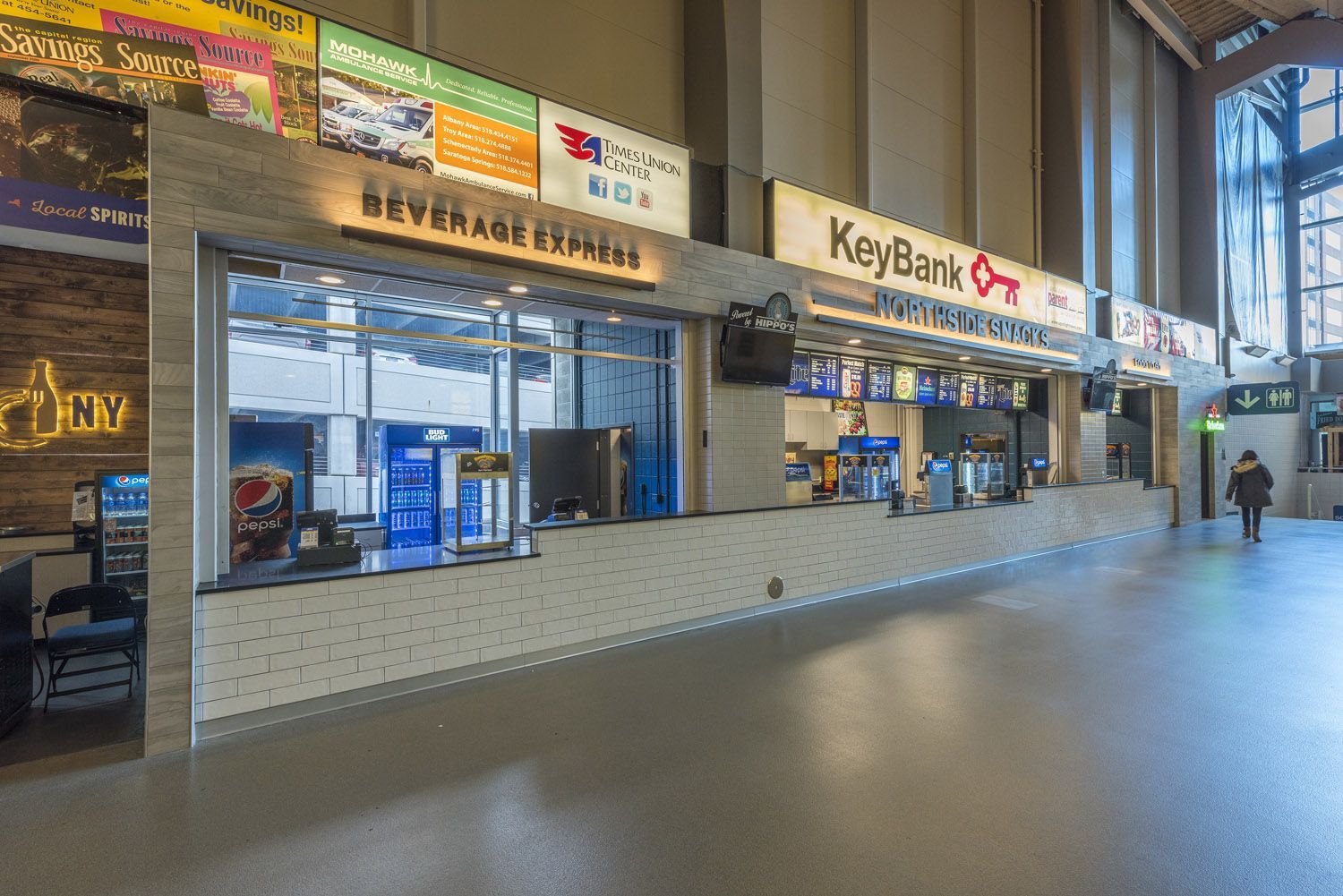 A Beverage Express and KeyBank concession stand with menu signs in an indoor venue, with a person walking in the distance.