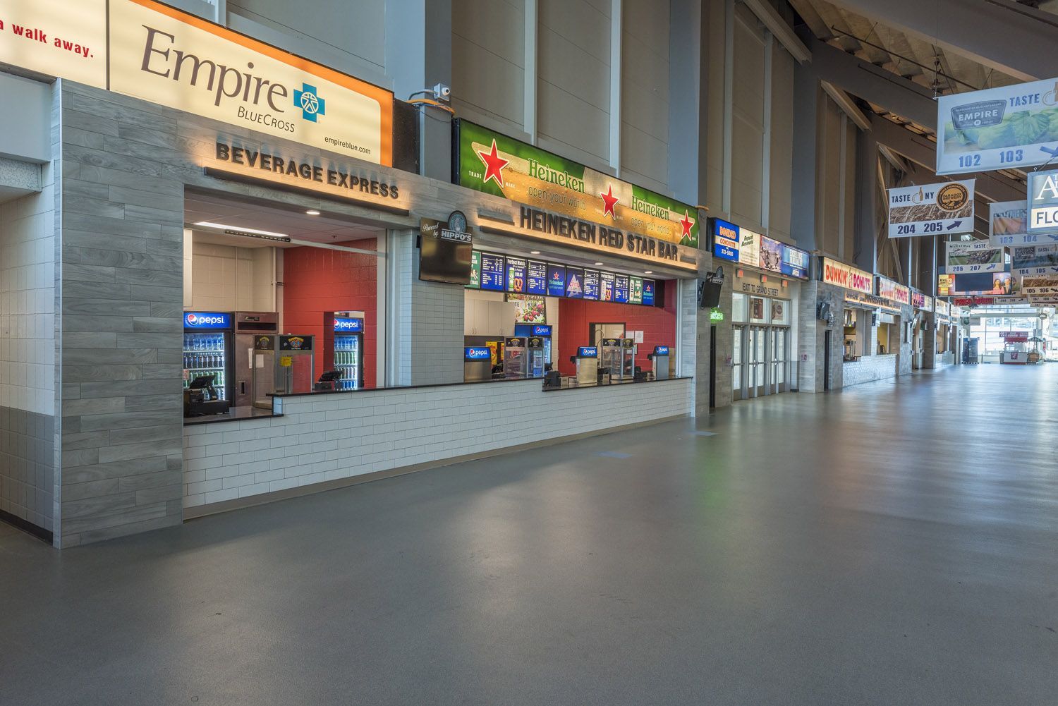A wide, empty stadium concourse featuring concession stands with signs for 