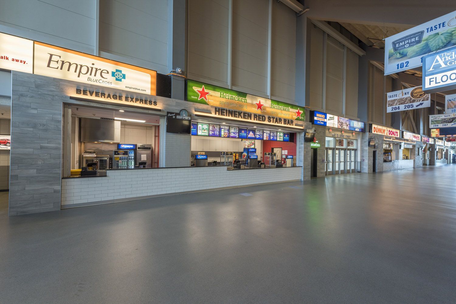A wide hallway with a row of food and beverage concession stands under bright lights in a modern arena or concourse.