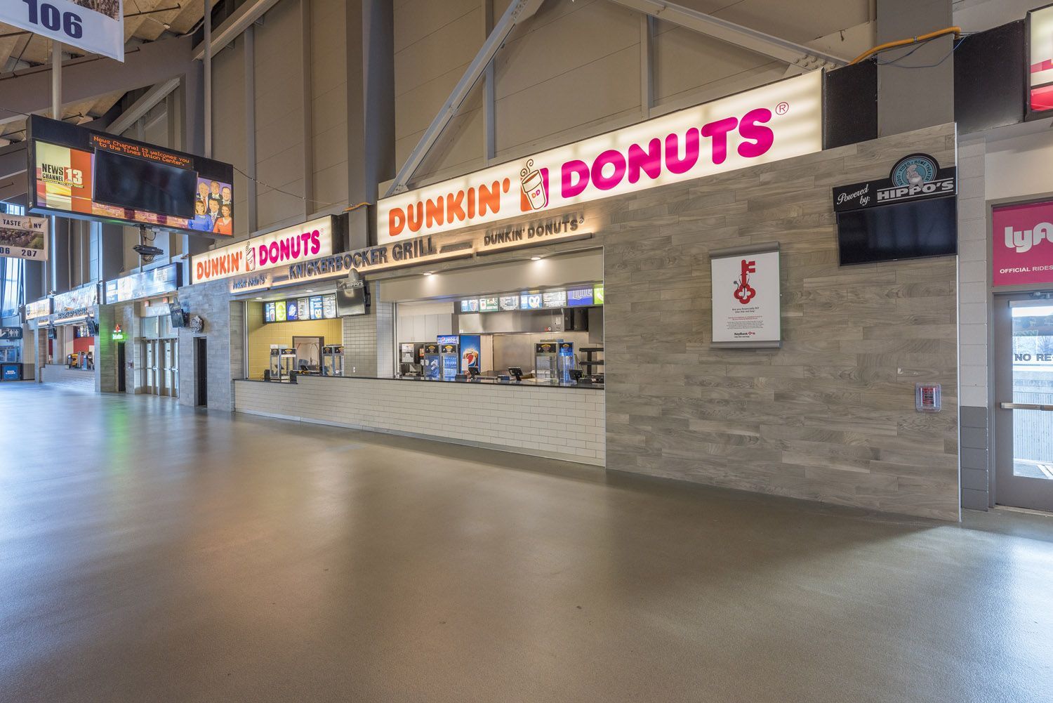 A Dunkin' Donuts concession stand in an empty, indoor stadium concourse with light-colored tile walls and floors.