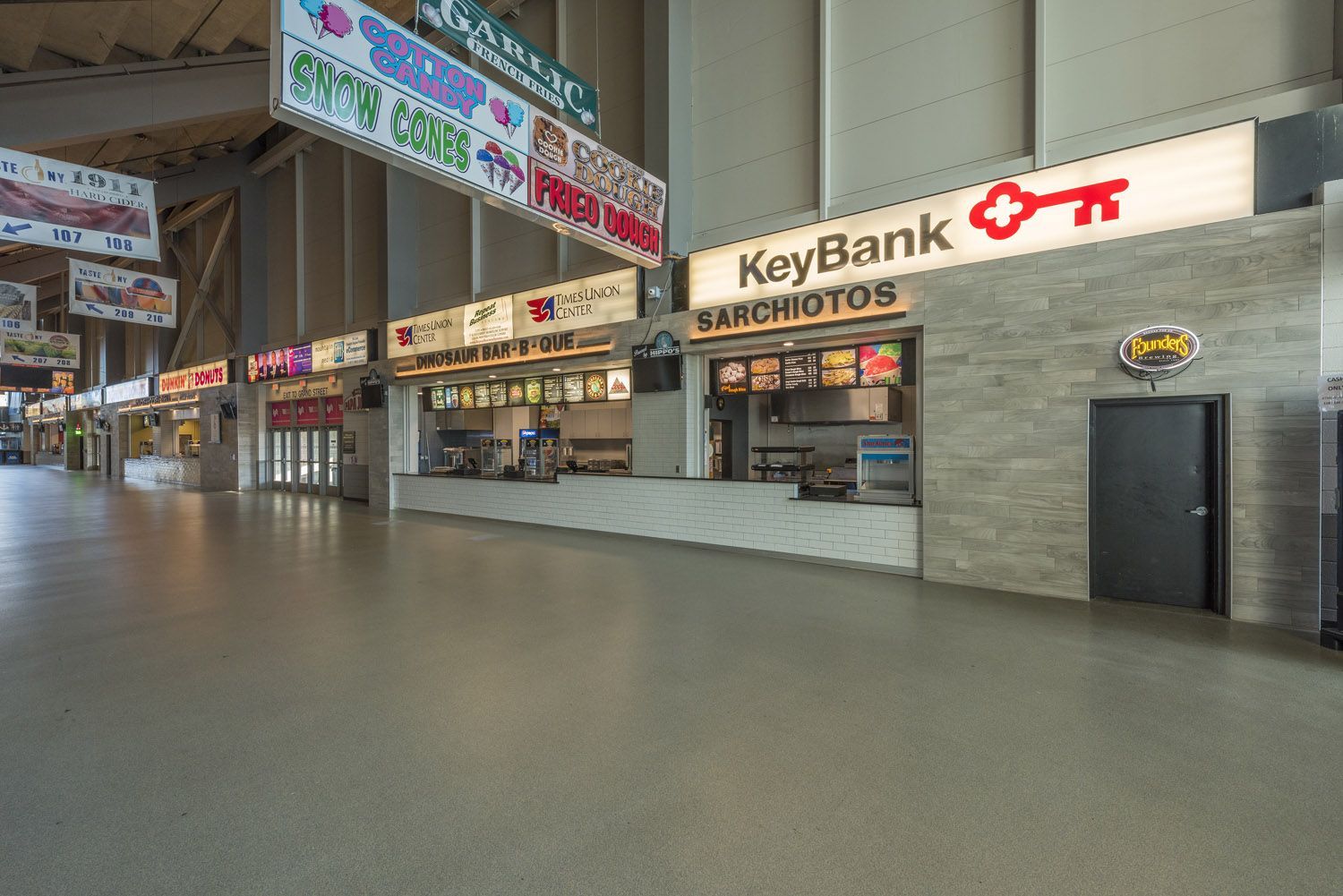 An empty stadium concourse lined with various concession stands and a KeyBank sign, with a light-colored, stone-like wall.