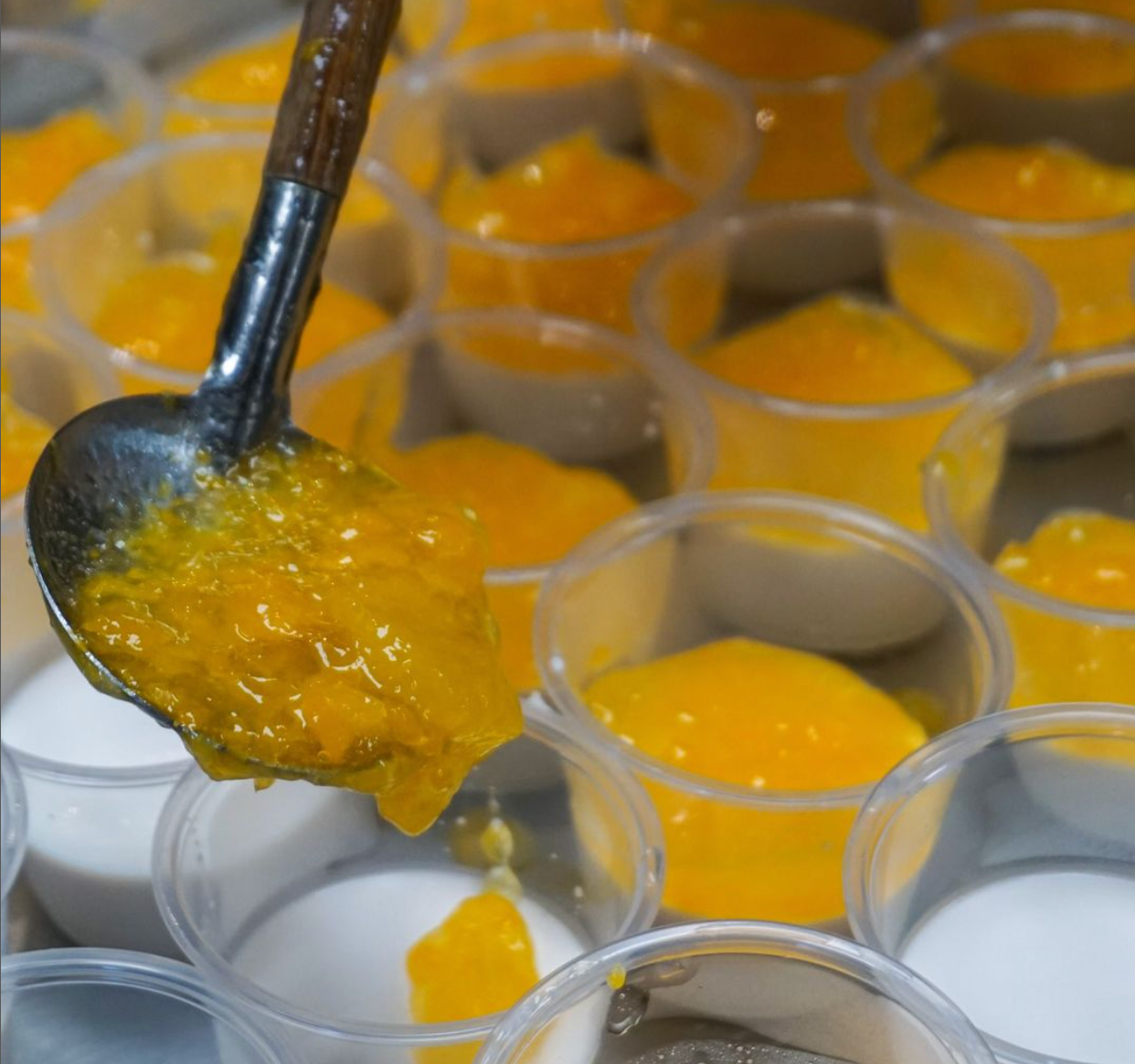 A spoonful of yellow sauce is being poured into a cup